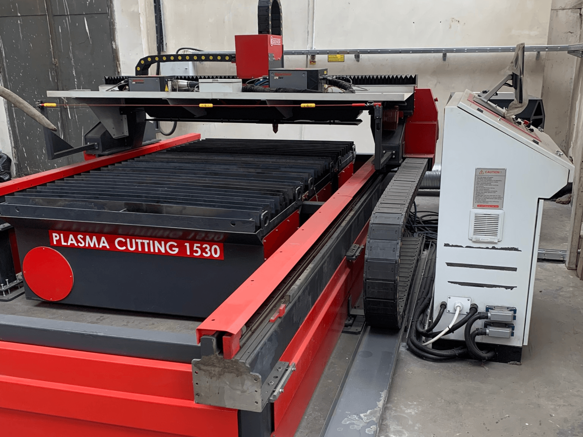 Machine de découpe au plasma DENER PL 1530, vue de profil montrant la table de découpe, le panneau de commande et les raccordements électriques.