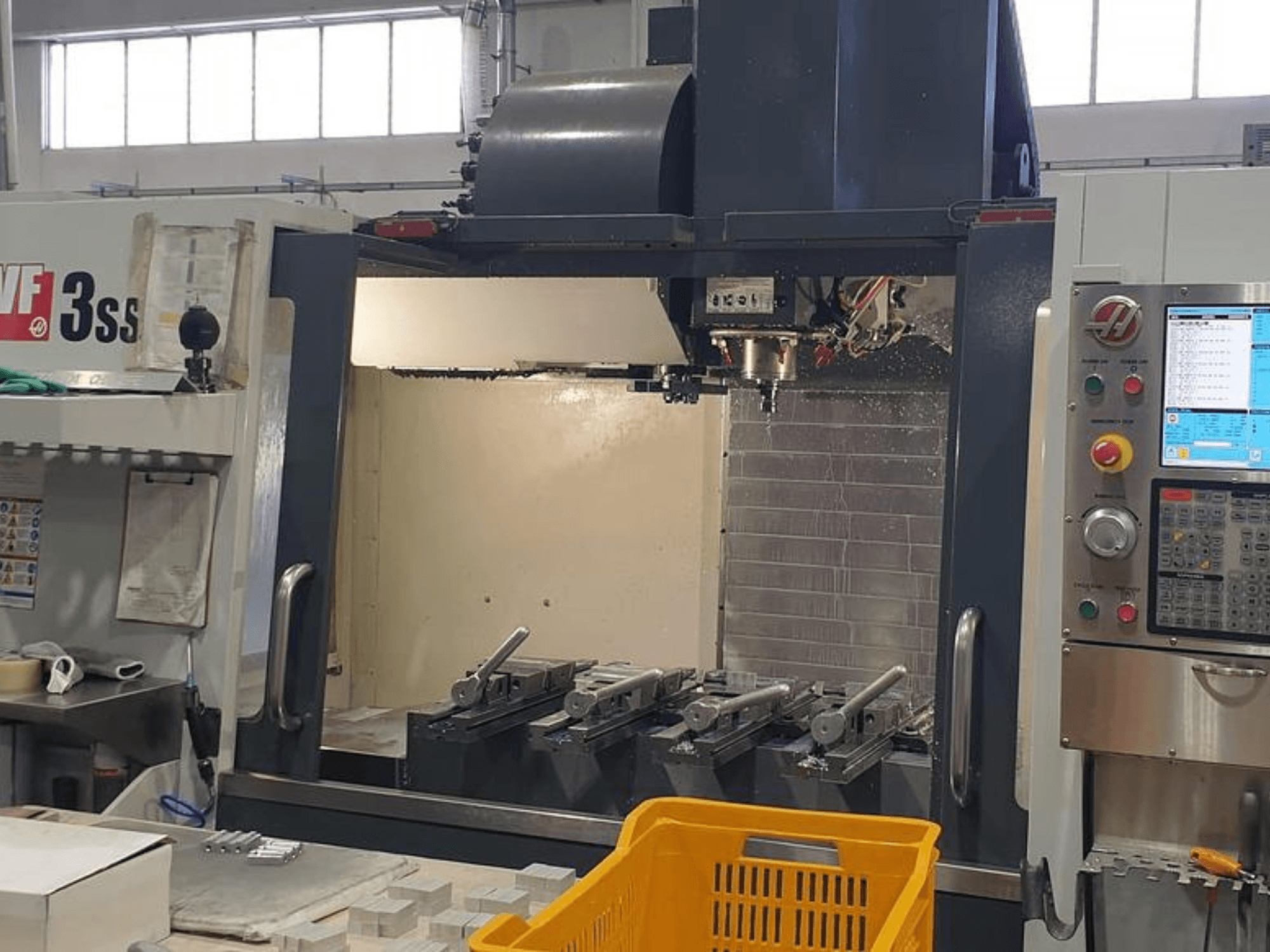 Centre d'usinage vertical HAAS VF-3SS, vue de face avec le panneau de commande CNC, les outils et le panier orange.