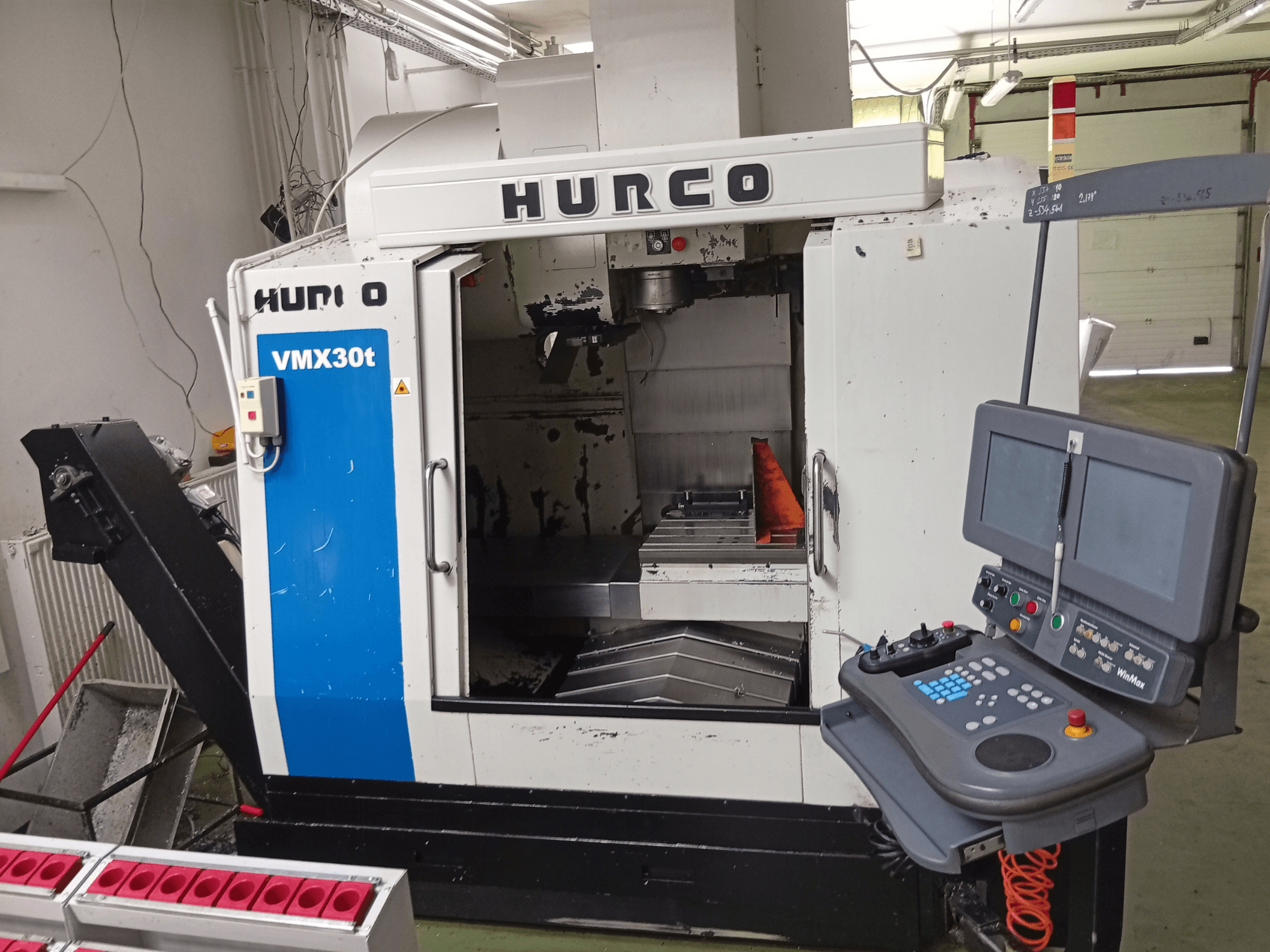 Centre d'usinage vertical Hurco VMX 30T, vue de face, présentant le panneau de commande et la zone de la broche avec la table de travail visible.