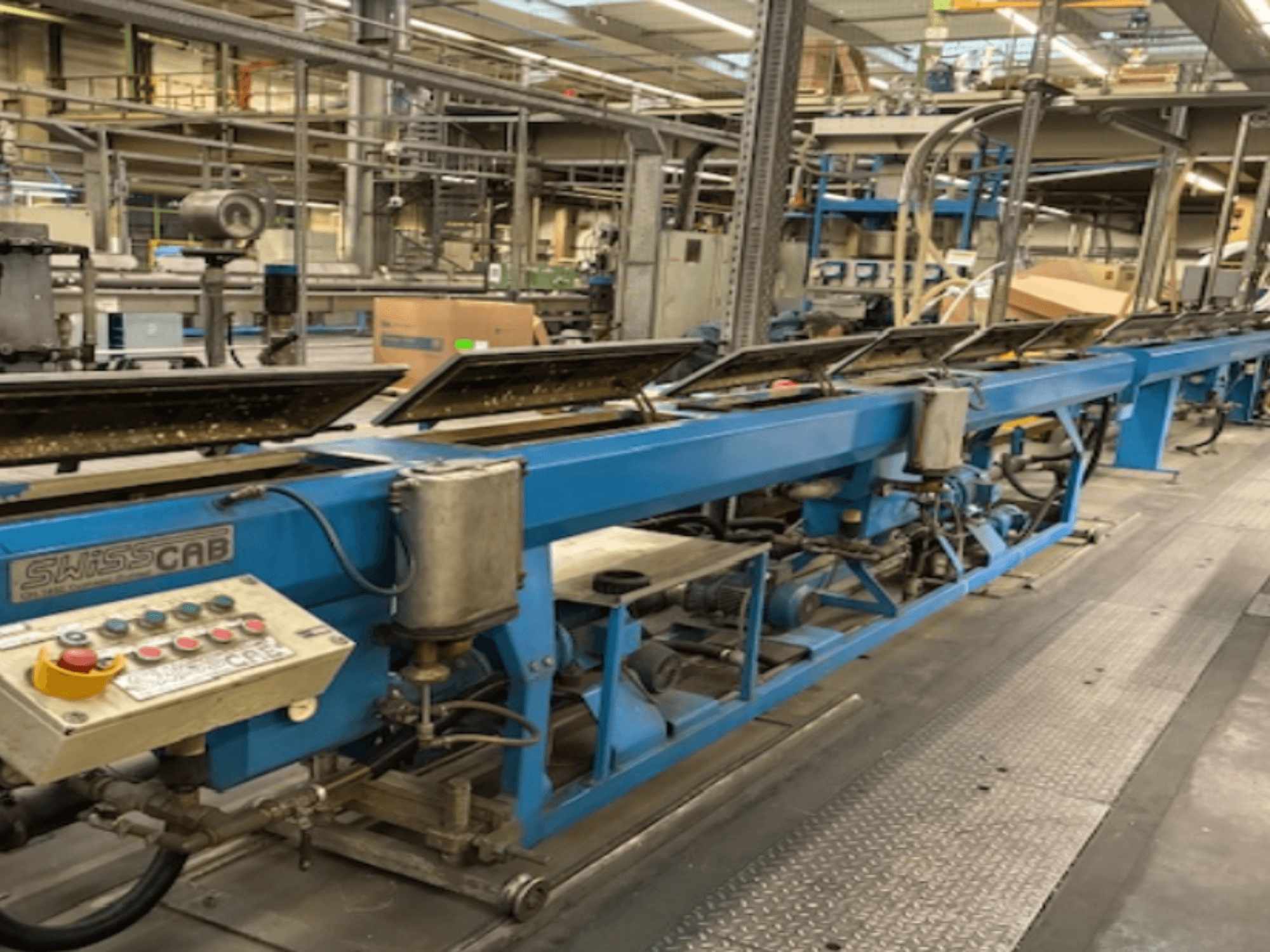 Machine industrielle SwissCab bleue dans une usine, avec des boutons de commande et un système de convoyage, vue de côté.