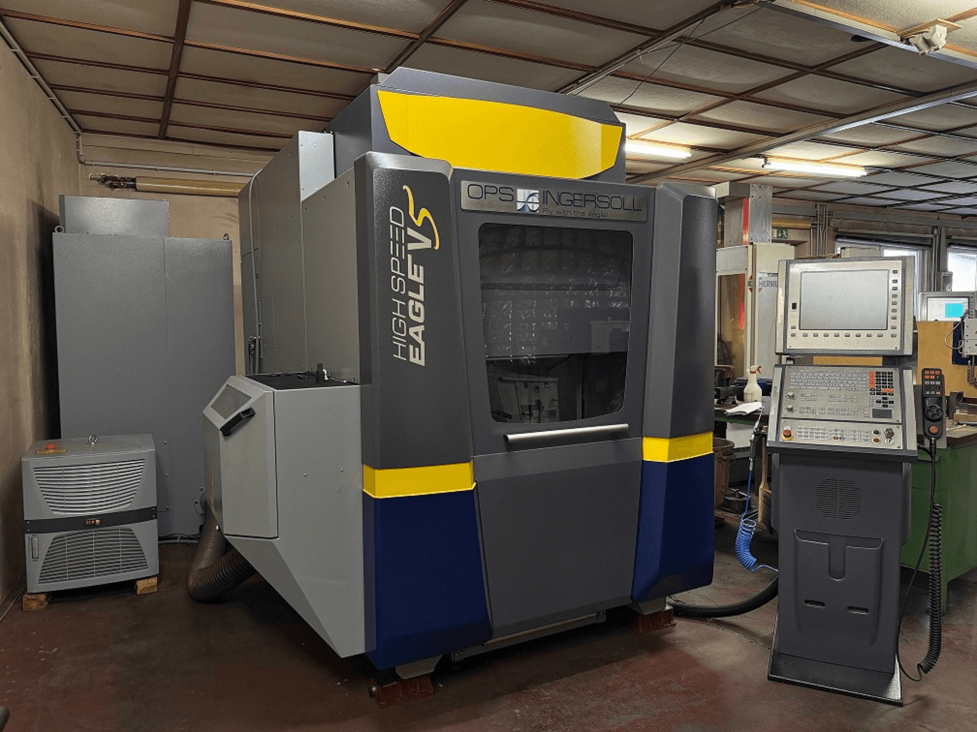 Machine Eagle V à grande vitesse d'OPS Ingersoll, vue de côté, avec panneau de commande et équipement adjacent dans un environnement industriel.