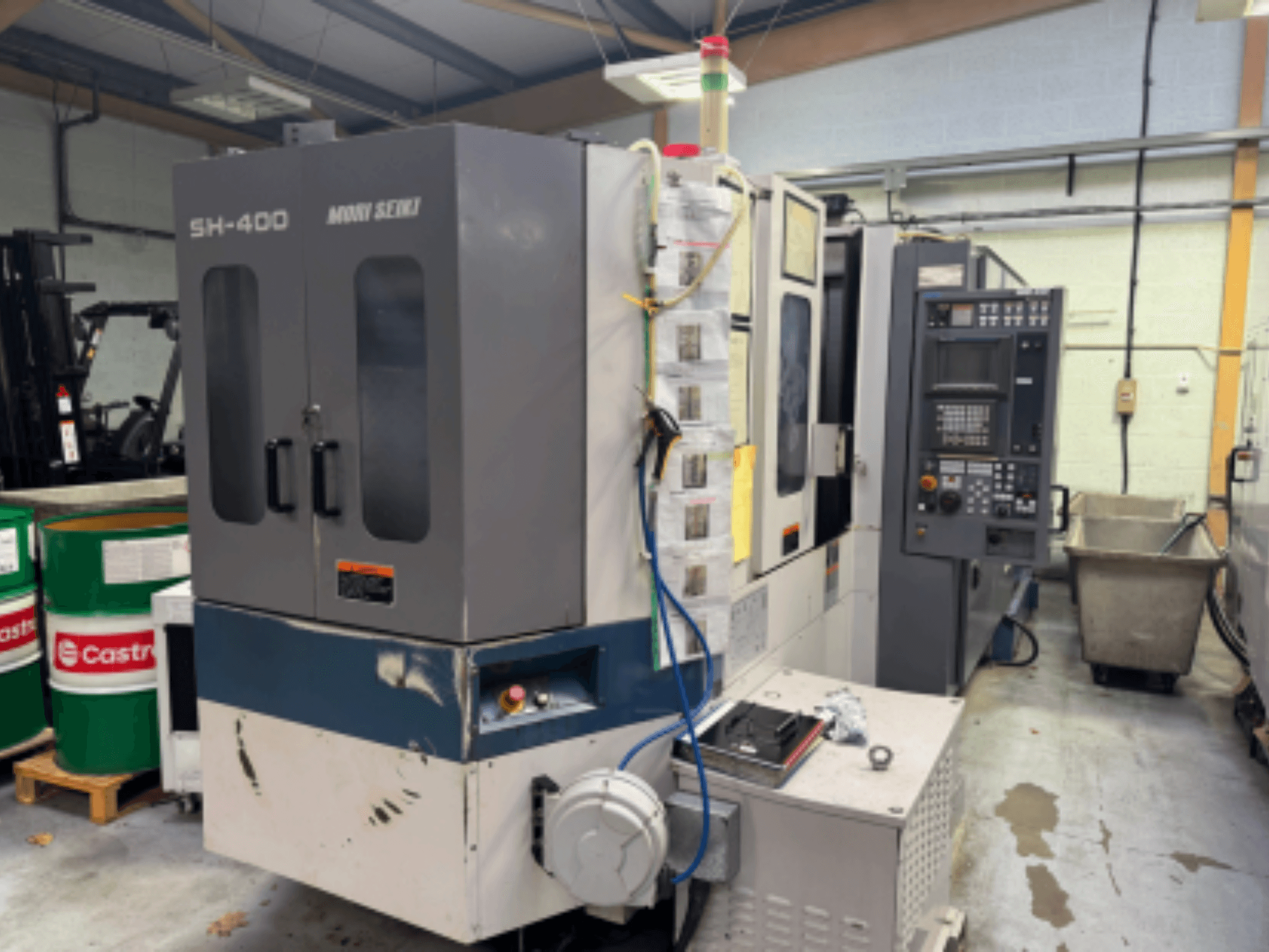 Machine CNC Moni Seiki SH-400, vue latérale montrant le panneau de commande, les portes et l'environnement industriel.