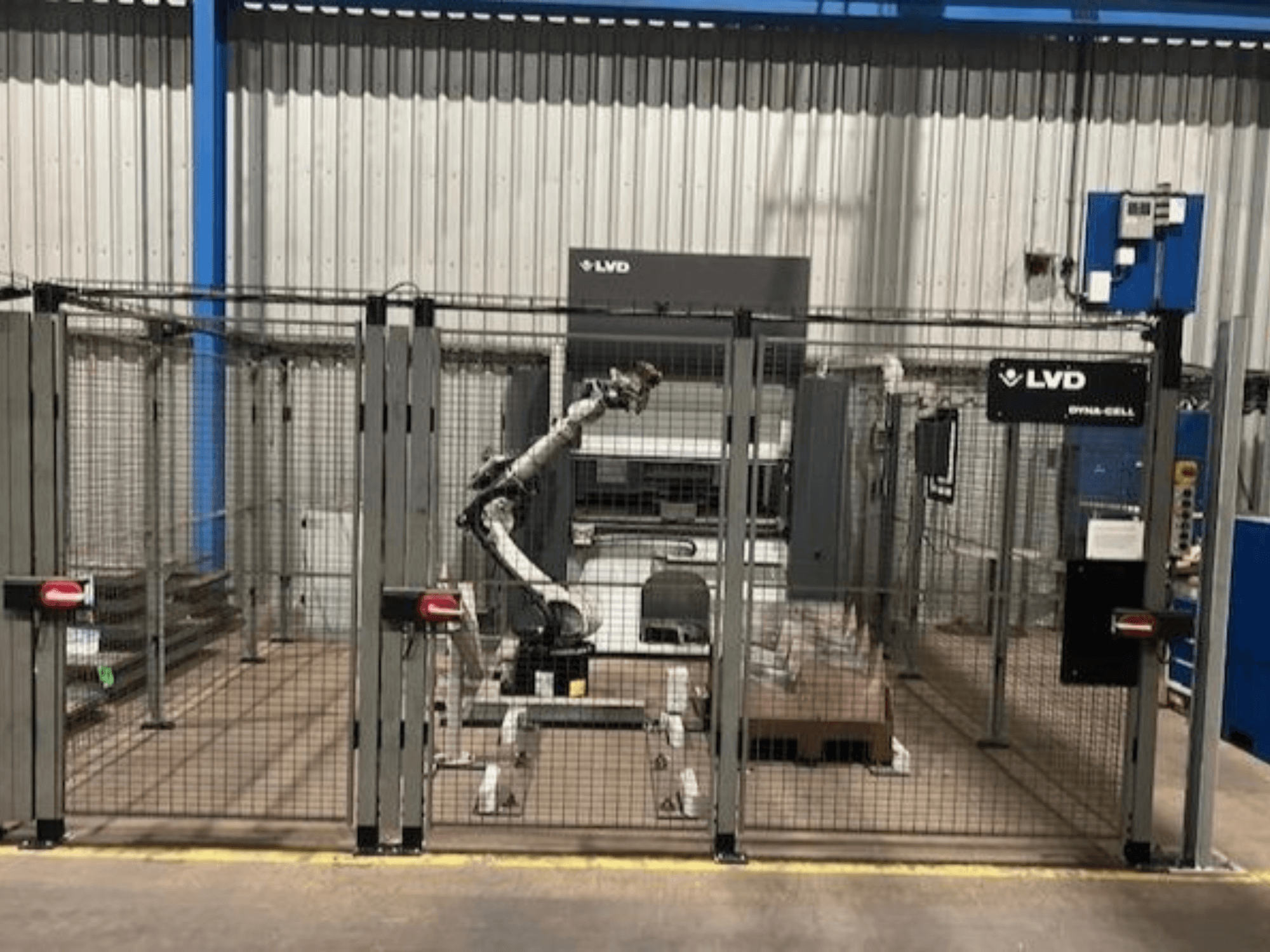 Station de travail robotisée LVD Dyna-Cell dans une enceinte clôturée, vue de face, avec le bras robotique et le panneau de commande.