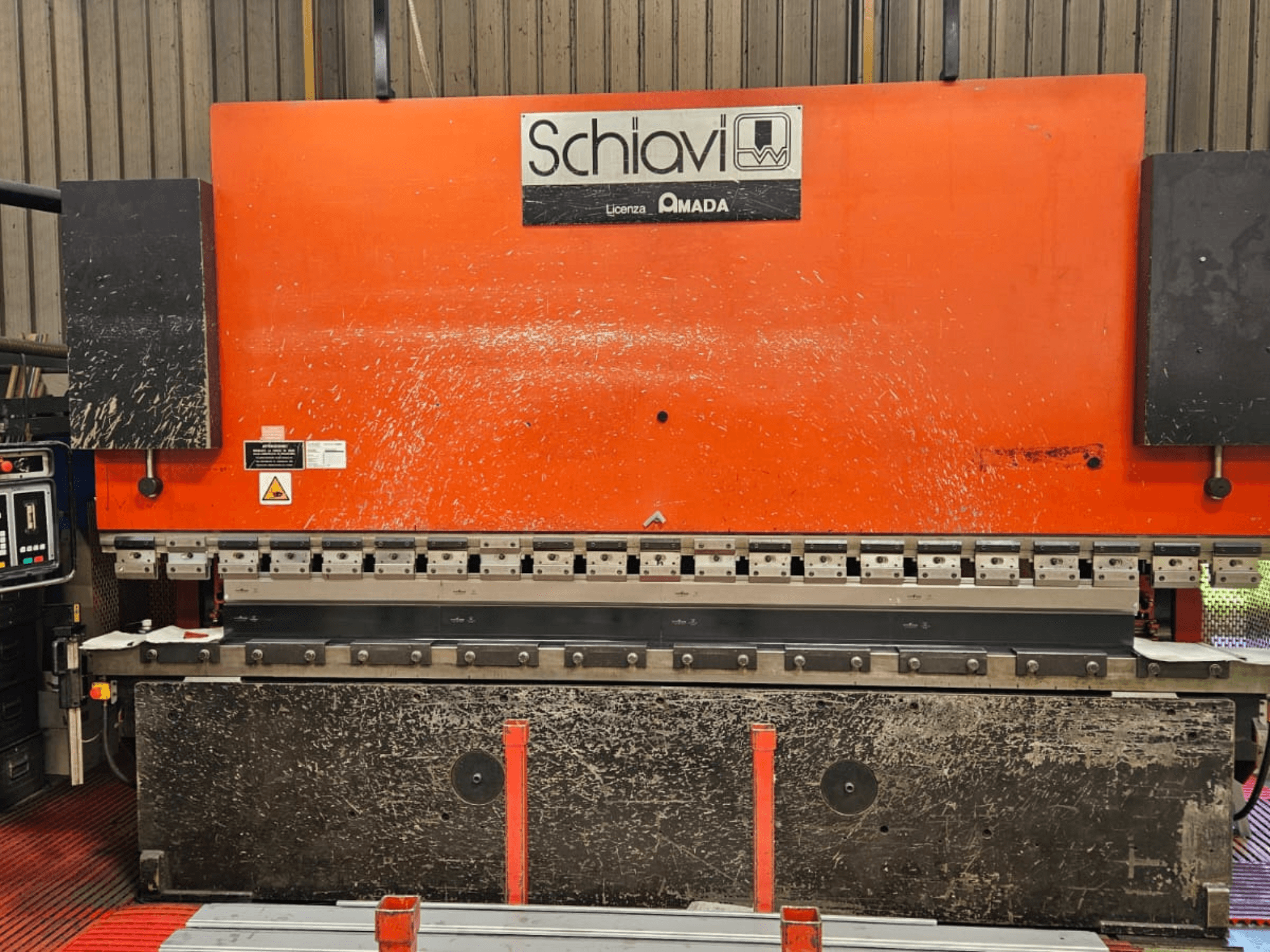 Machine à plier les métaux Schiavi Amada, vue de face, avec corps orange, panneau de commande à gauche, et plusieurs outils de pliage visibles.