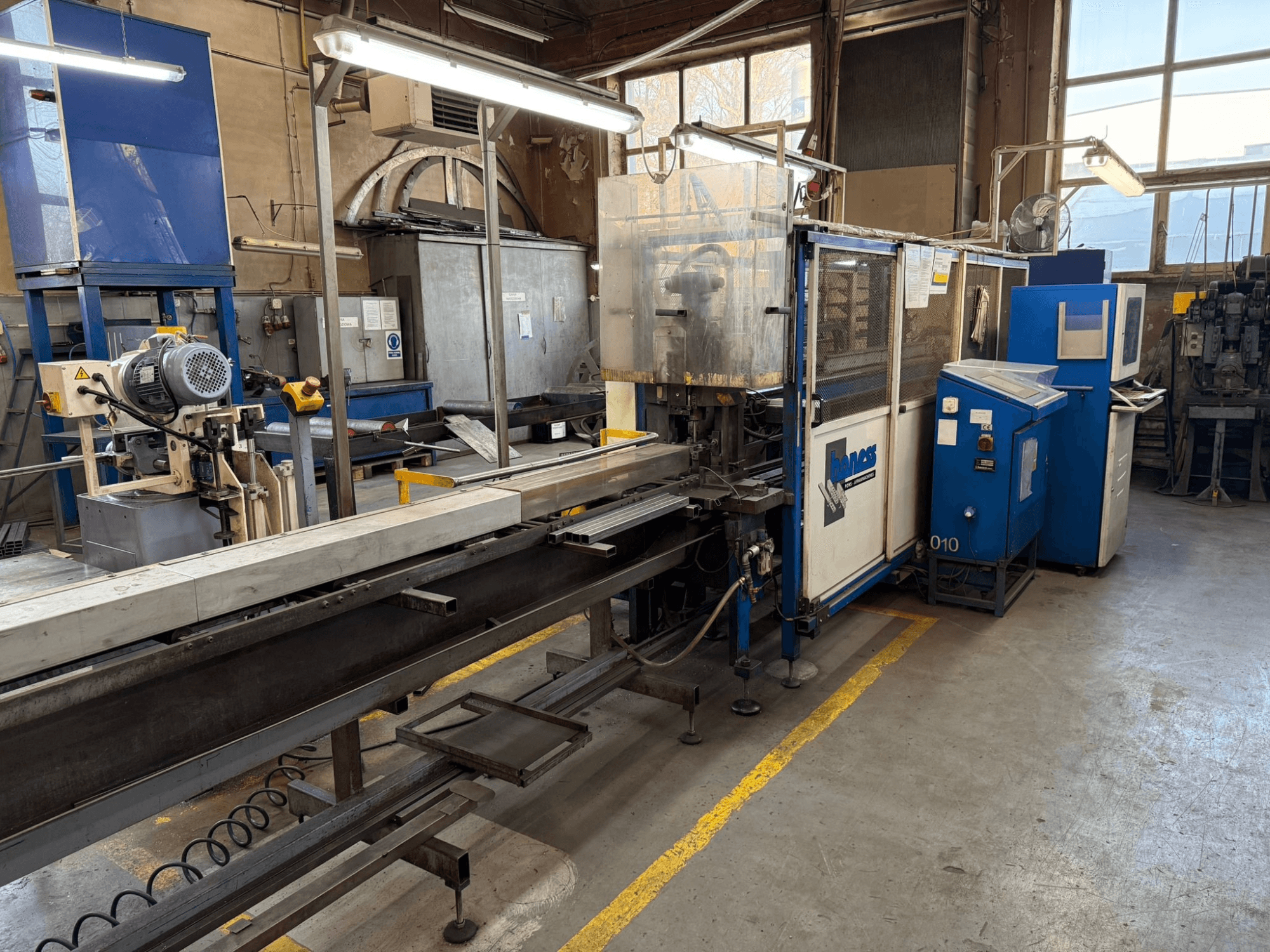 Atelier industriel avec une machine Haweas bleue, vue de côté montrant le convoyeur et l'équipement dans un grand espace bien éclairé.