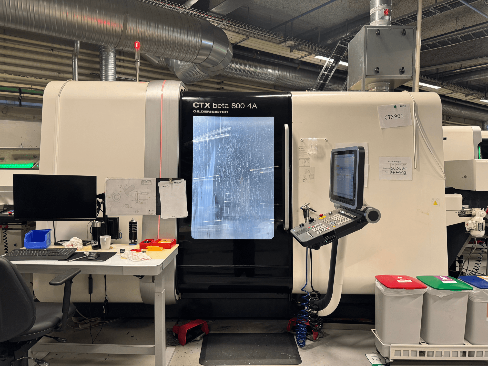 Machine CTX beta 800 4A avec panneau de commande et moniteur, vue de côté, dans un atelier avec bureau et poubelles colorées.