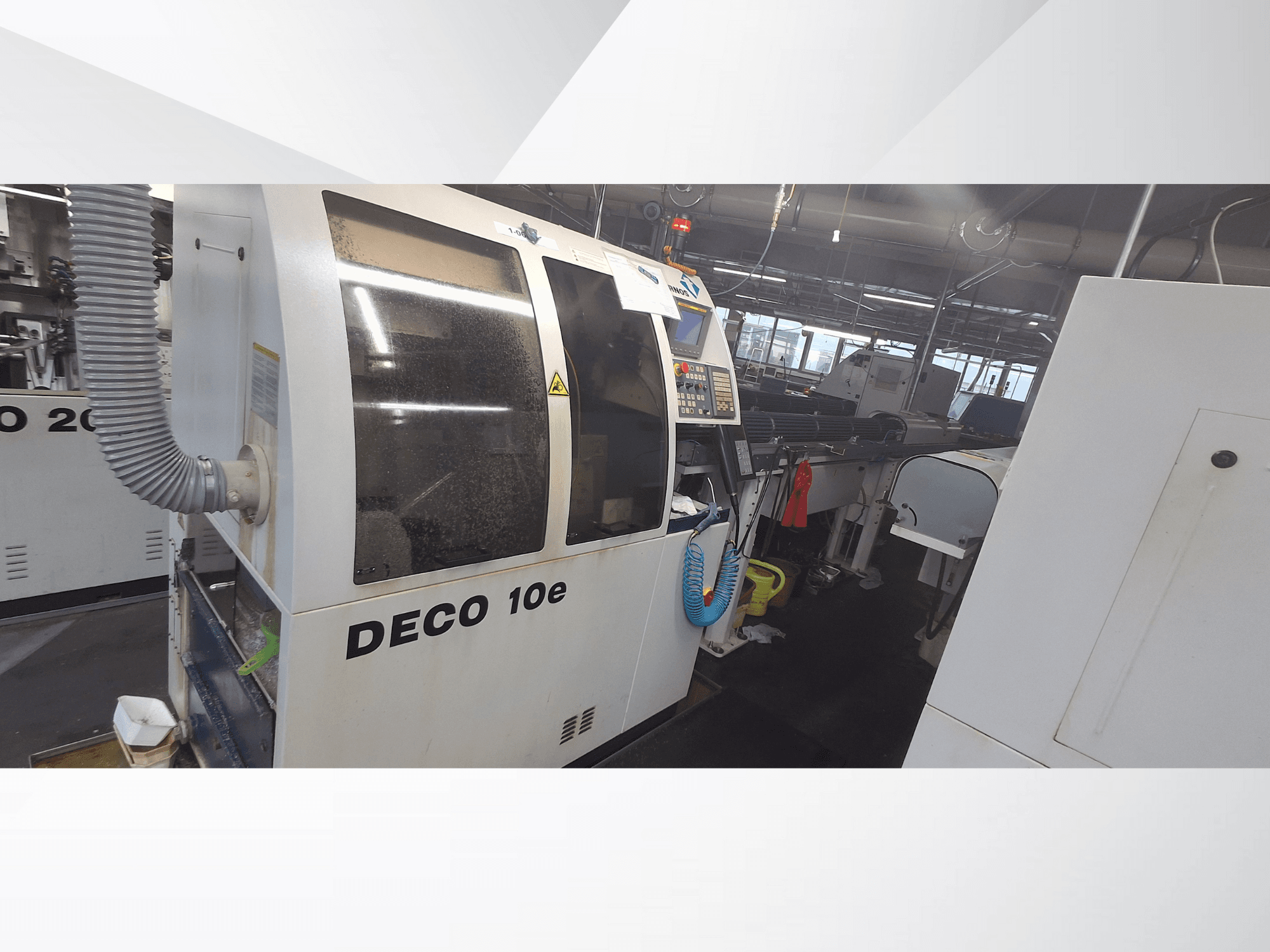 Machine DECO 10e dans un atelier ; vue latérale montrant le panneau de commande et le tuyau de ventilation, avec des machines floues à l'arrière-plan.