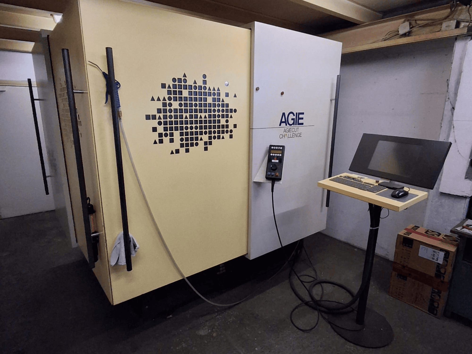 Machine d'électroérosion à fil AGIE Agiecut Challenge 2 dans un atelier, avec panneau de commande et écran posés sur un support, vue de face.