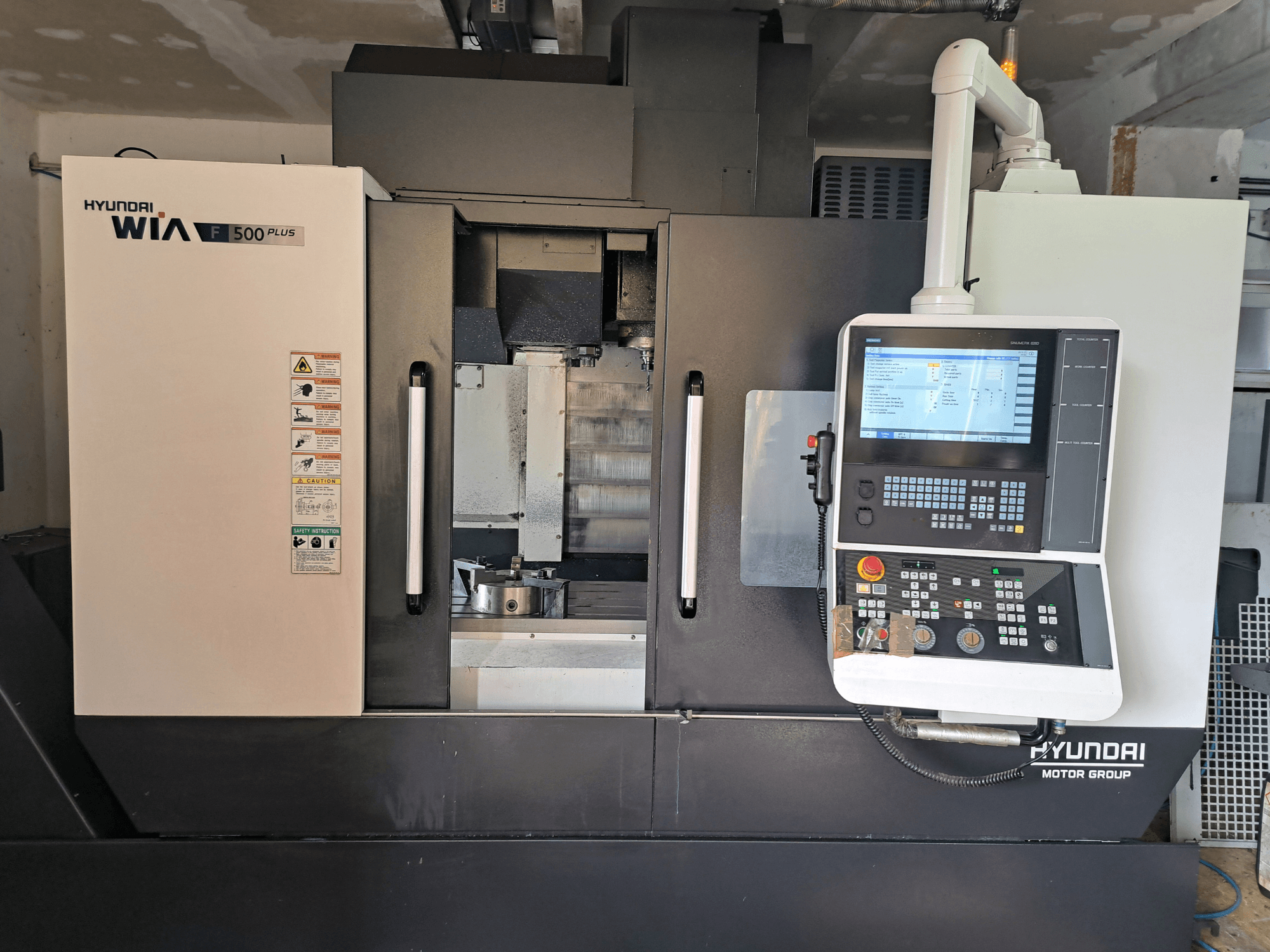 Machine CNC Hyundai WIA F500 Plus vue de face, dotée d'un panneau de commande numérique et d'étiquettes de sécurité.