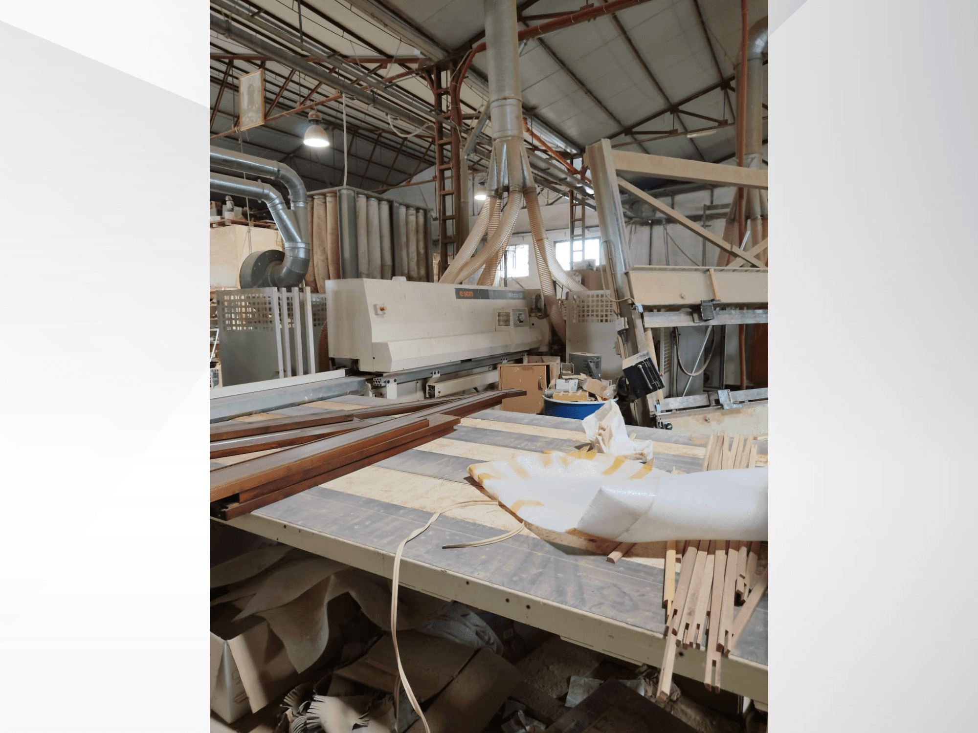 Centre d'usinage du bois CNC SCM Windor60 dans un atelier, vu de côté avec des panneaux de bois et un équipement d'extraction de la poussière.