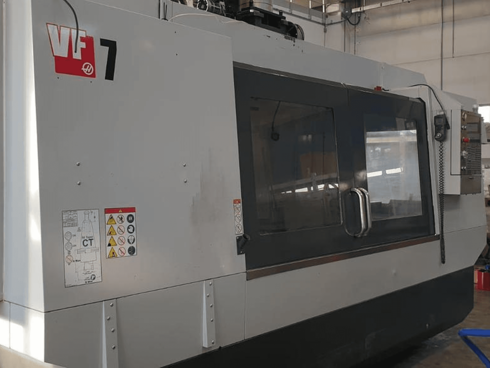 Machine CNC Haas VF-7 vue de côté, présentant une finition gris métal, un panneau de commande et des étiquettes de sécurité.