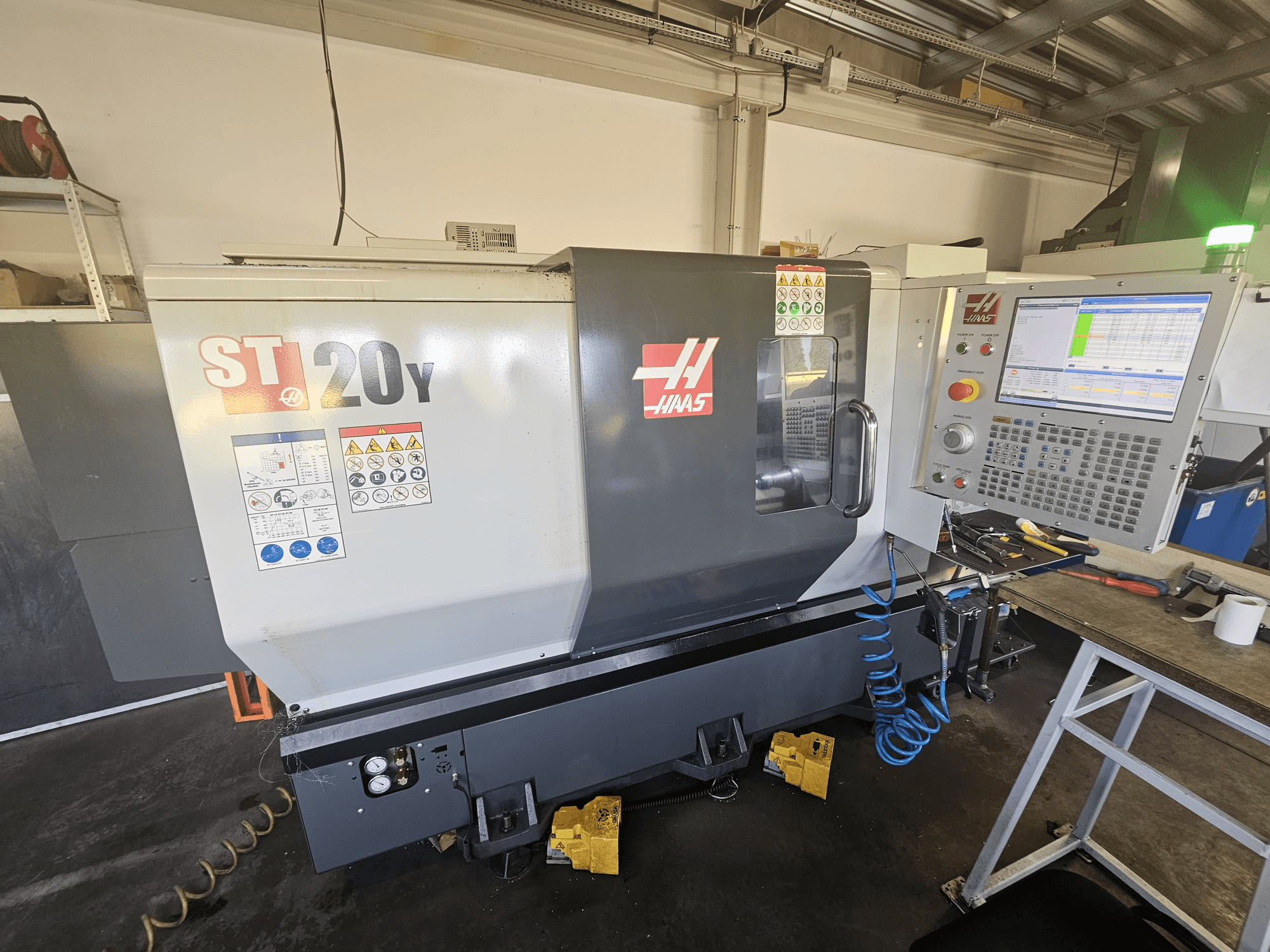 Tour CNC Haas ST-20Y vu de face avec le panneau de commande ; comprend les étiquettes de sécurité et le détail du tuyau d'air sur le côté.