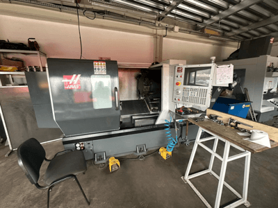 Tour CNC Haas (modèle ST-10) dans un atelier, vue latérale montrant les commandes, les outils sur un établi et une chaise à proximité.