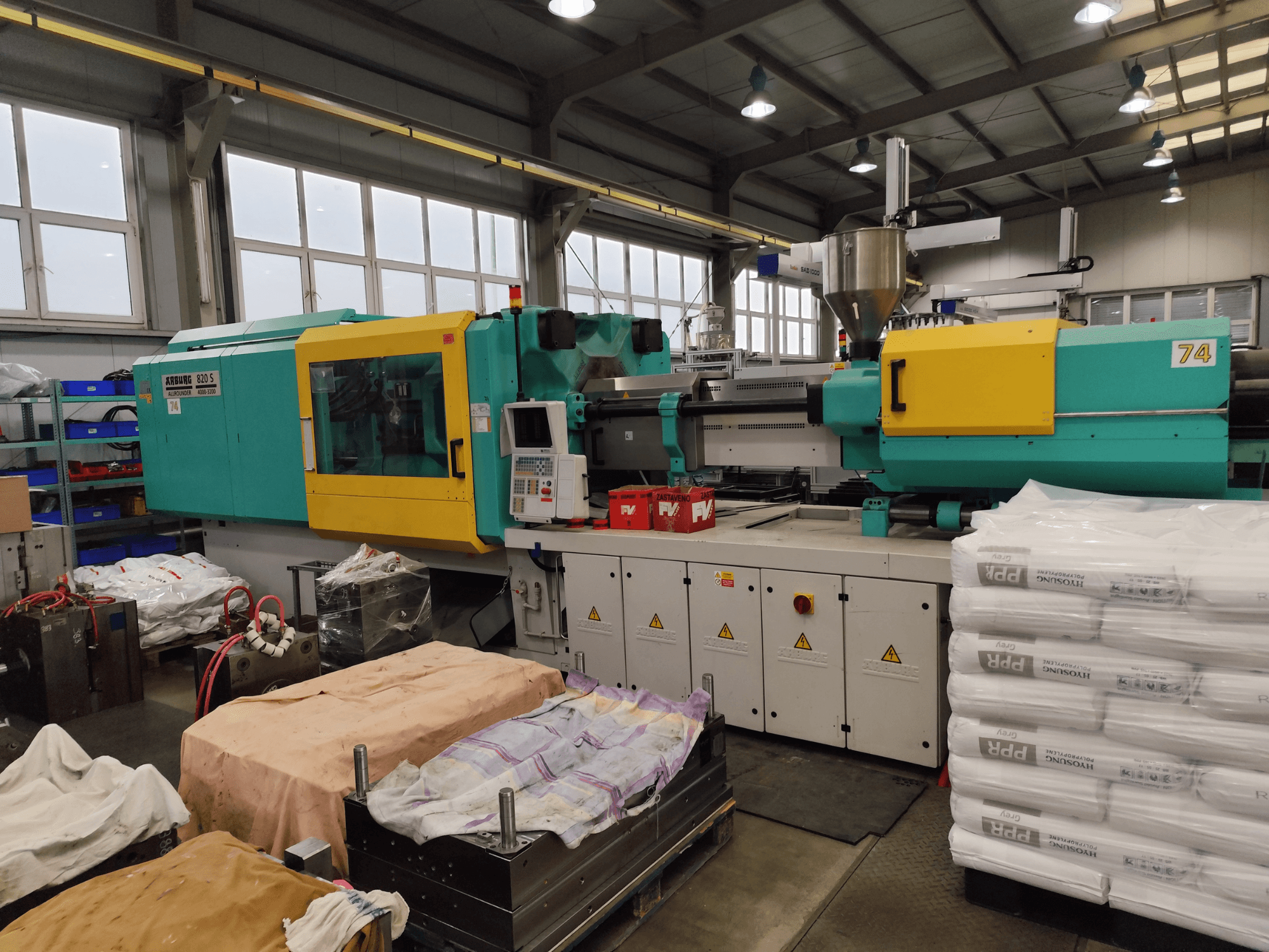 Machine de moulage par injection d'Arburg, vue de face, extérieur jaune et sarcelle, avec l'outillage et les matériaux à proximité.
