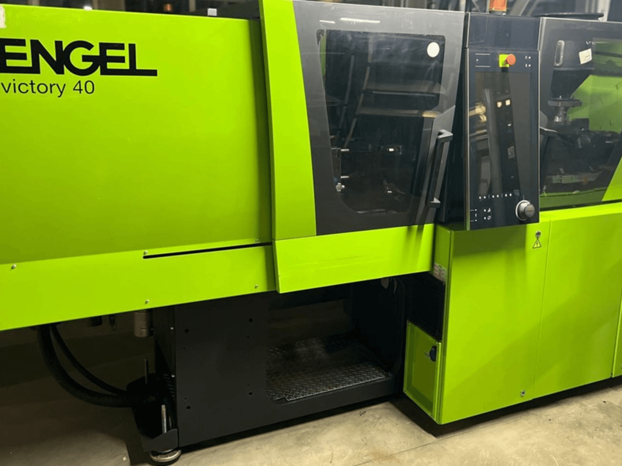Machine de moulage par injection ENGEL Victory 40 en vert brillant, vue de face montrant le panneau de commande et la porte d'accès avec l'étiquette d'avertissement.