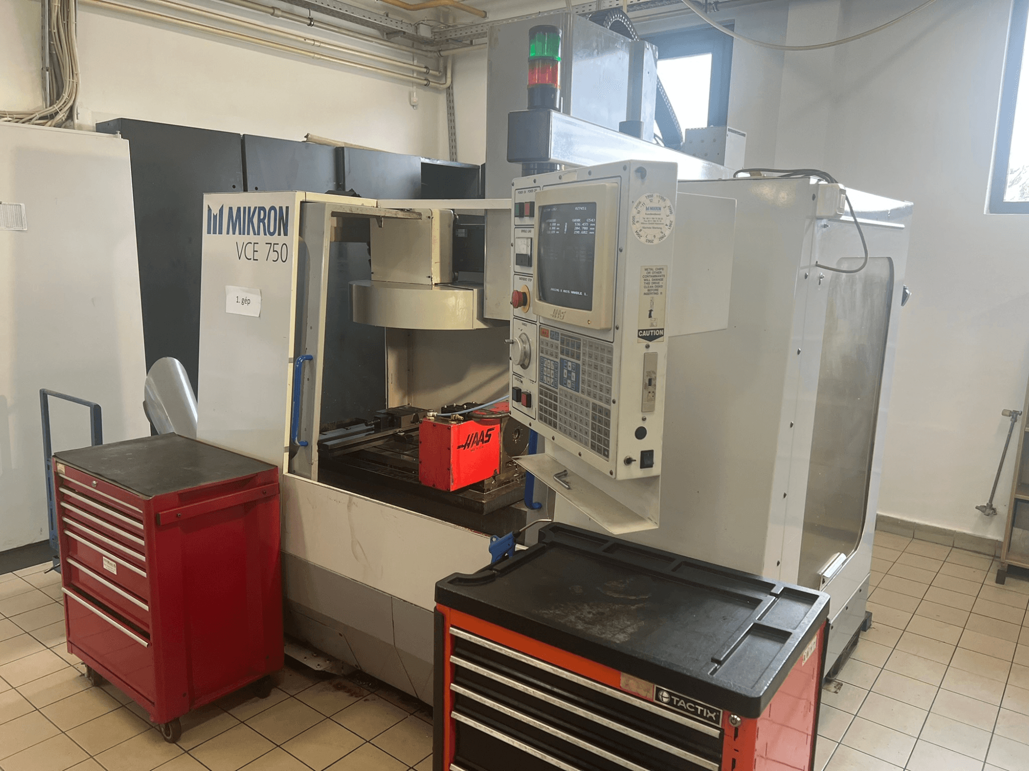 Alt text : "Centre d'usinage vertical MIKRON VCE 750, vue de face avec le panneau de commande et les boîtes à outils rouges, dans un atelier spacieux".