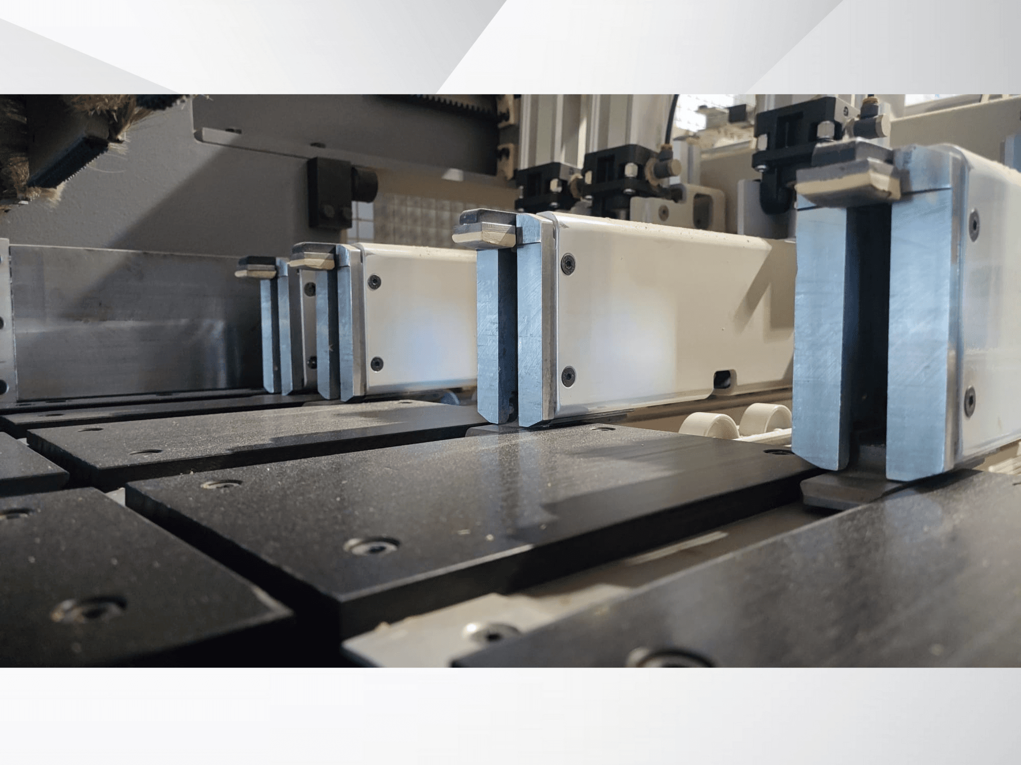 Vue rapprochée du mécanisme de serrage d'une machine de précision à mâchoires métalliques, avec des surfaces de travail noires et des rails de guidage visibles.