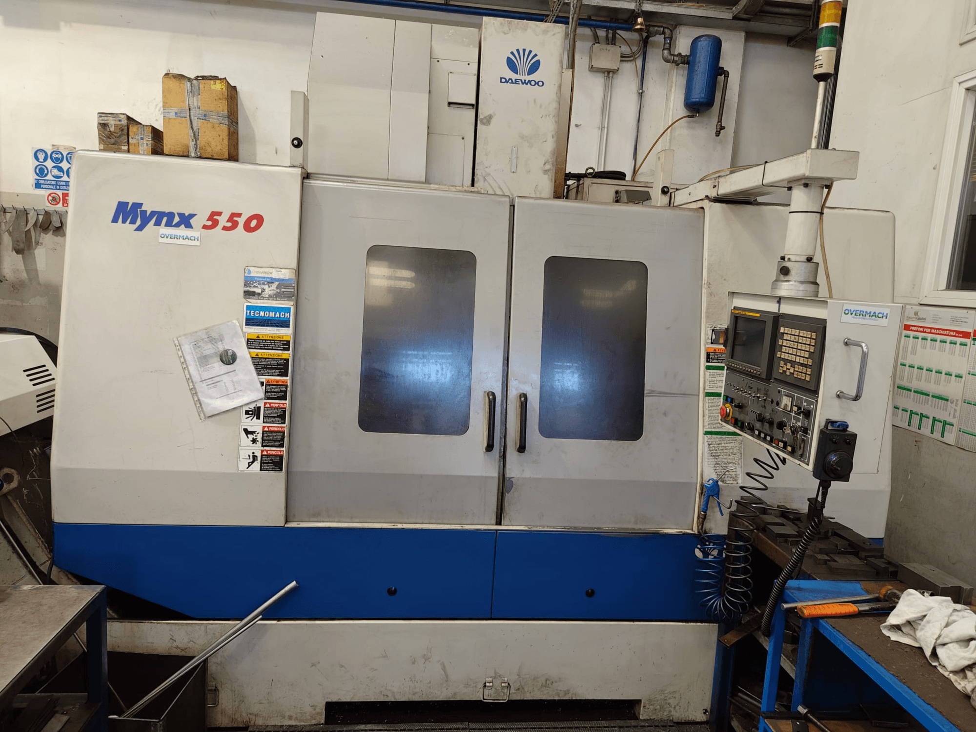 Centre d'usinage vertical DAEWOO MYNX 550, vue de face, avec le panneau de commande, deux grandes portes et des étiquettes de sécurité.