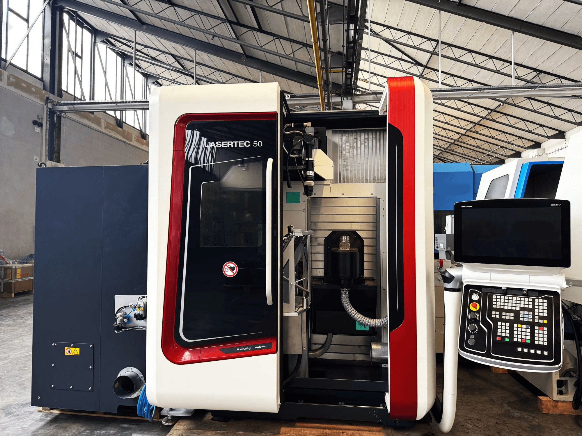 Machine CNC LaserTec 50 vue de côté, avec un panneau de commande en noir et blanc, un porte-outil visible et un environnement industriel.