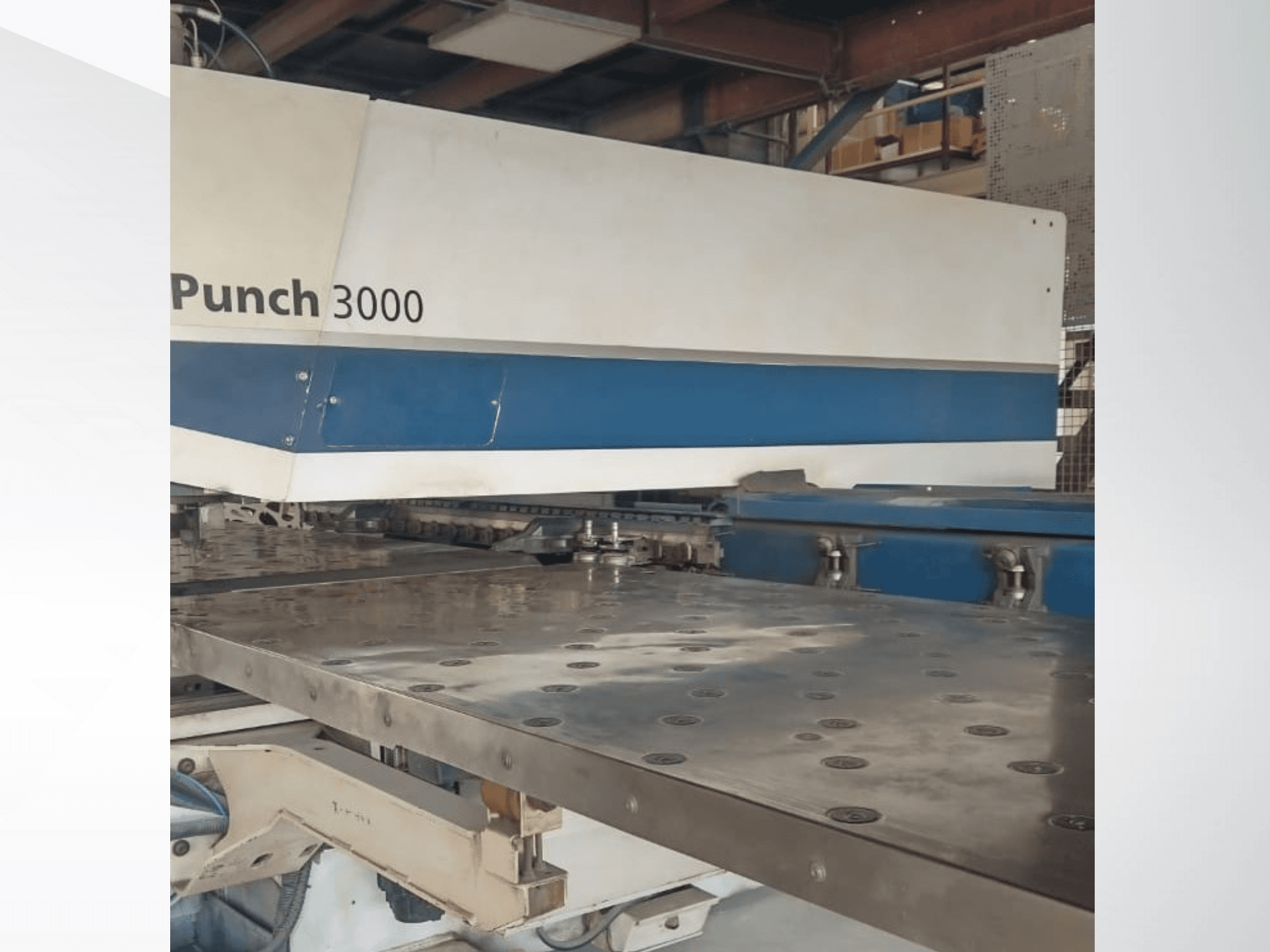 Machine à poinçonner 3000 dans un atelier, vue de face, montrant une grande surface métallique plate avec plusieurs trous de poinçonnage.