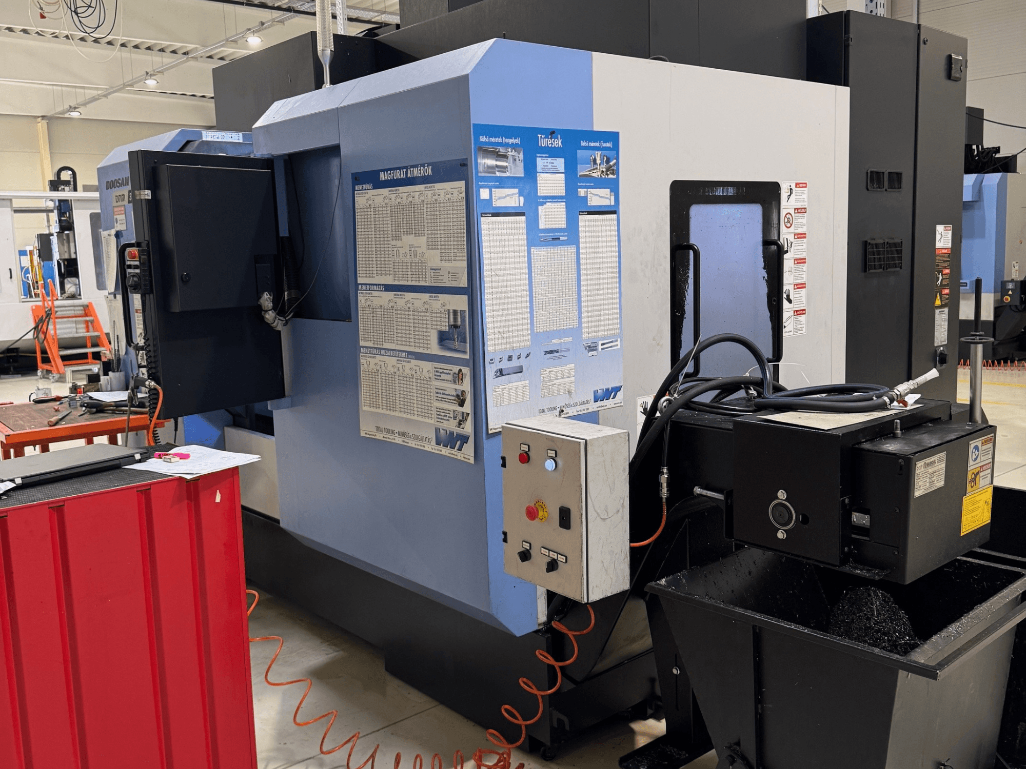 Centre de fraisage-tournage DOOSAN DNM350/5AX, vue latérale montrant le panneau de commande et le réservoir de liquide de refroidissement, avec des détails de fonctionnement visibles.
