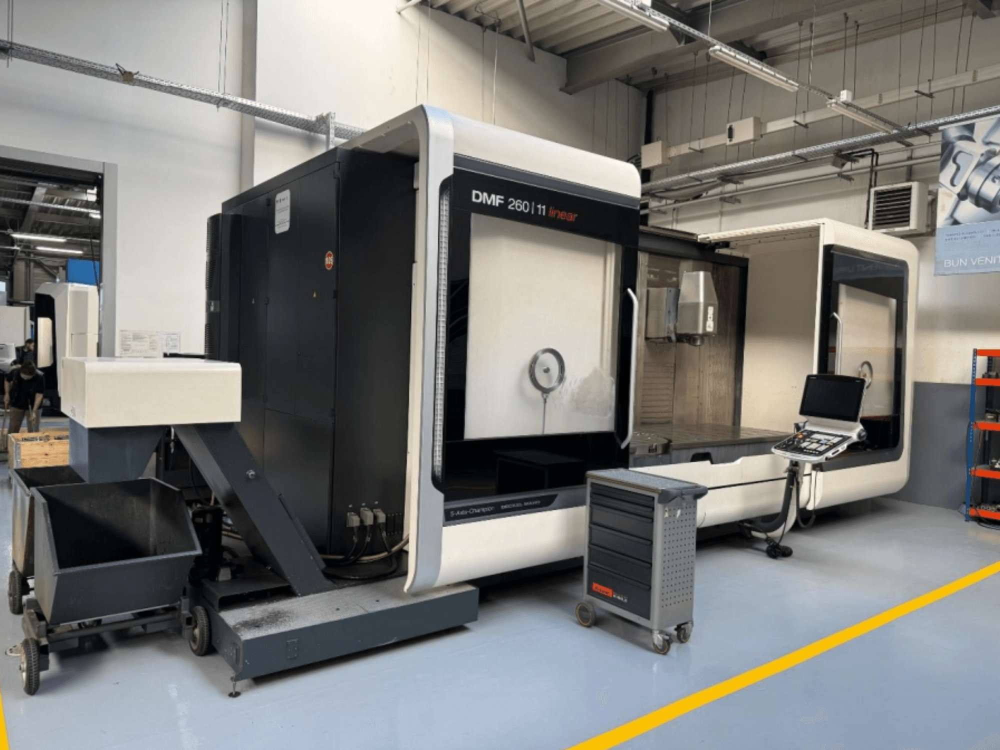 Fraiseuse linéaire DMF 260 de DMG MORI présentée de face, avec un panneau de commande d'outils et un chariot d'outils mobile à proximité.