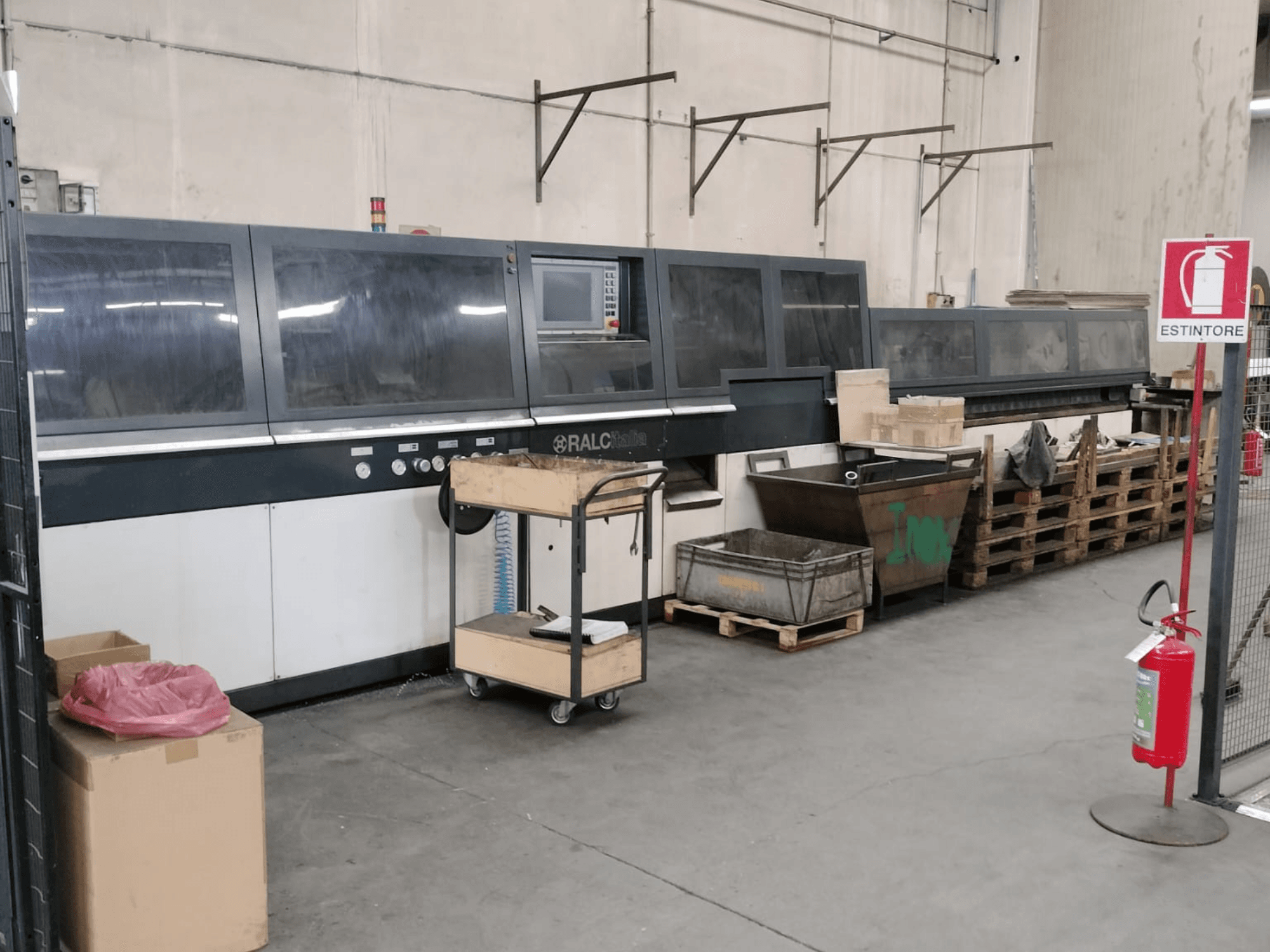 Machine industrielle RALC dans une usine, vue de face, panneau de commande visible ; palettes en bois et extincteur à proximité.