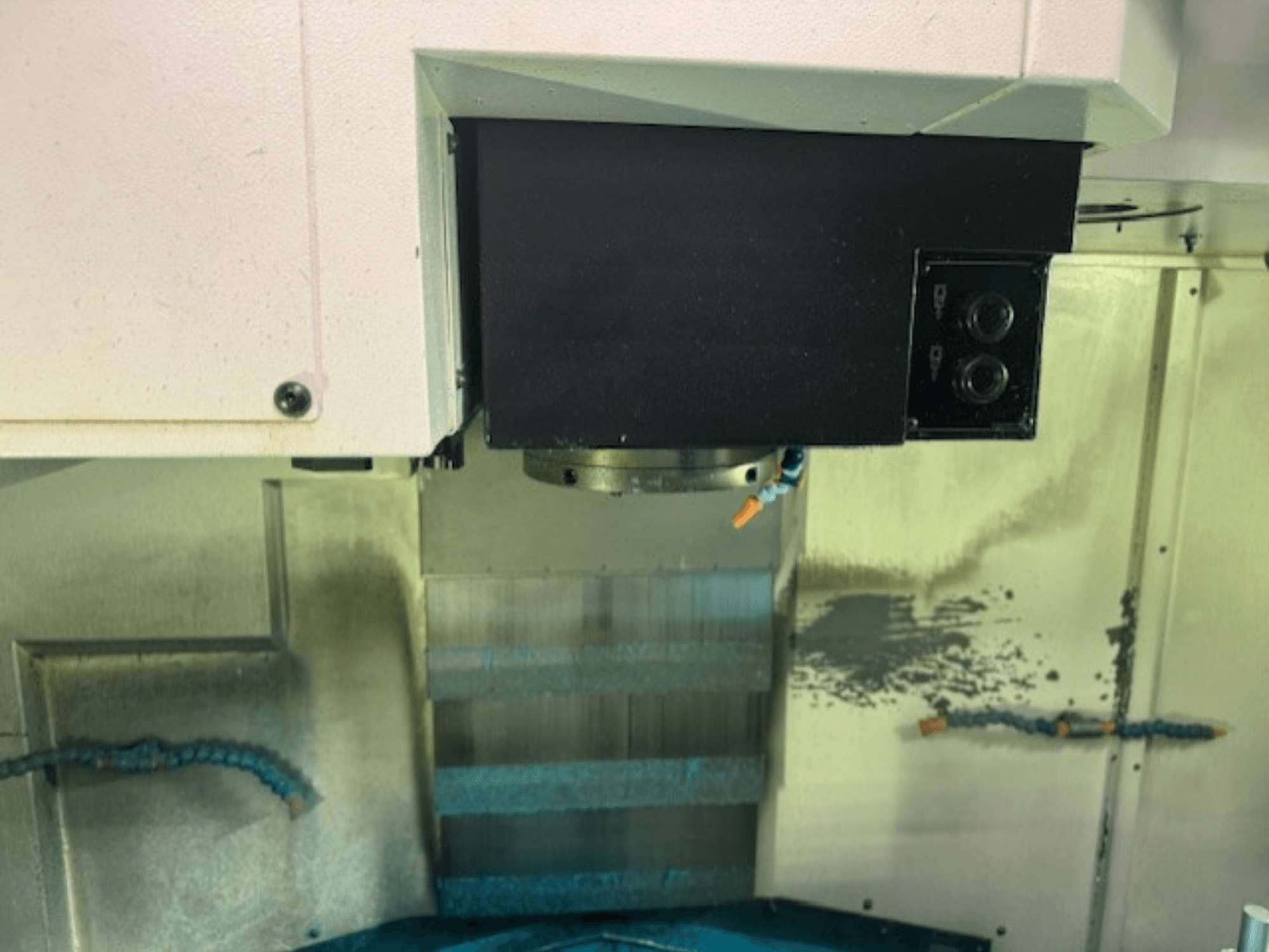 Gros plan sur le panneau de commande d'une fraiseuse CNC et sur le porte-outil, avec les détails de la marque, les boutons et la surface de travail.