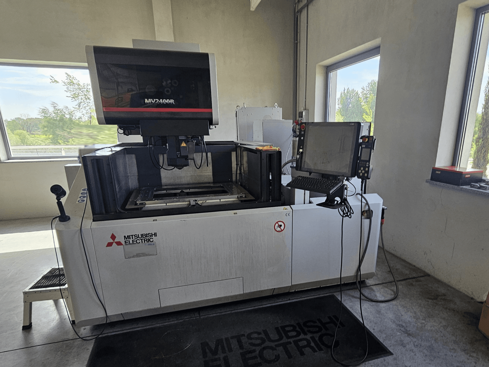 Machine d'électroérosion à fil MV2400R de Mitsubishi dans un atelier, avec un panneau de commande à écran tactile et un espace de travail.