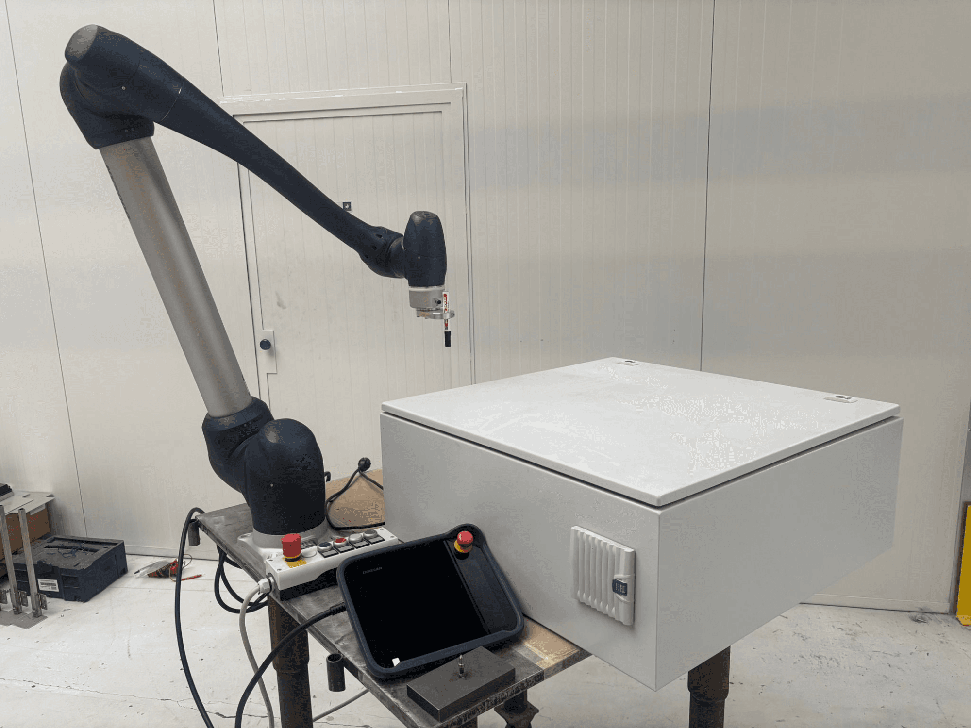 Robot collaboratif DOOSAN M0617 en vue latérale, avec le bras robotique étendu au-dessus d'une interface de contrôle et d'une boîte blanche sur une table.