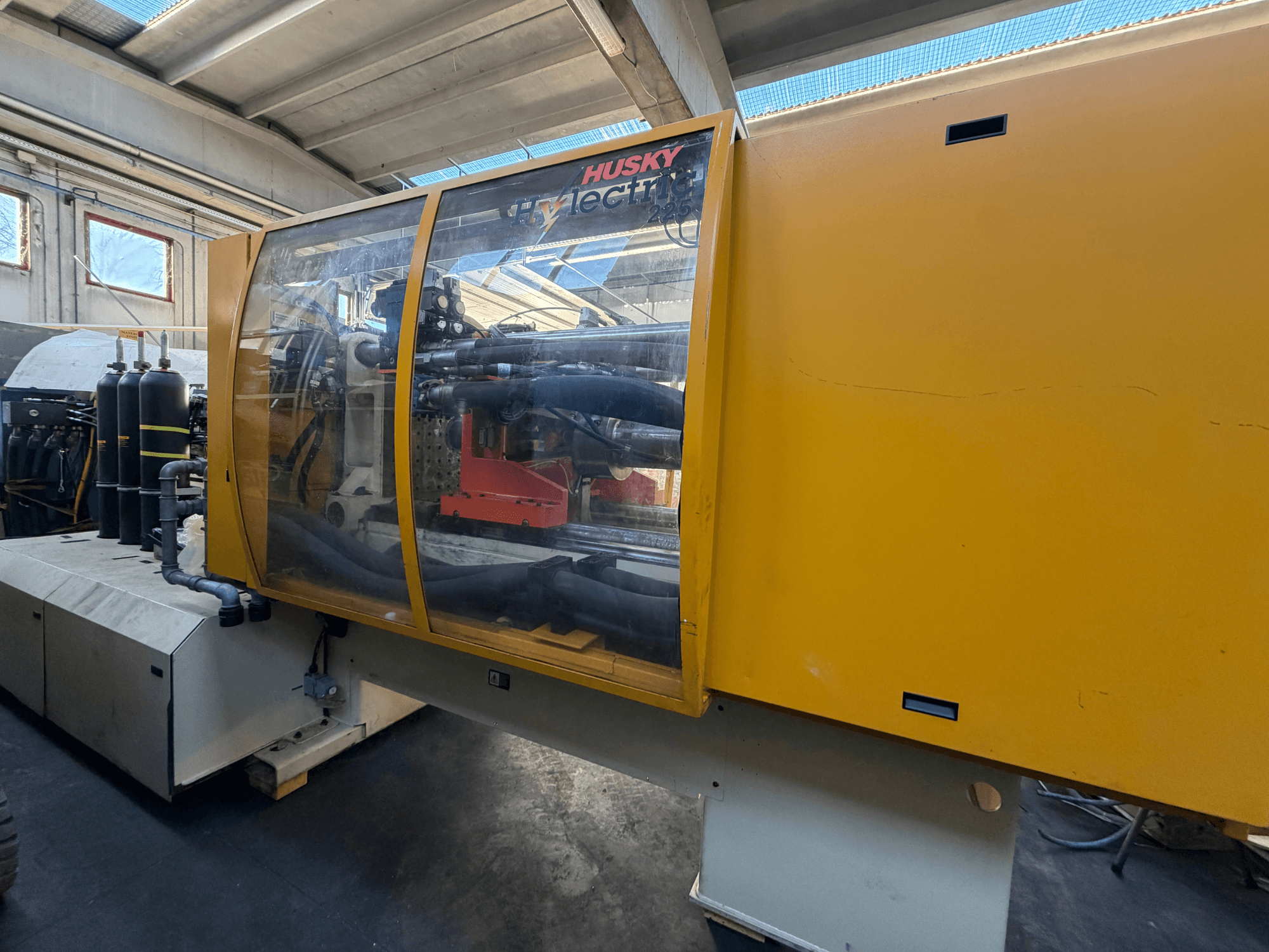 Machine à injecter électrique Husky HL225 RS65, vue de face avec le carter jaune, le panneau de commande visible et les composants hydrauliques.