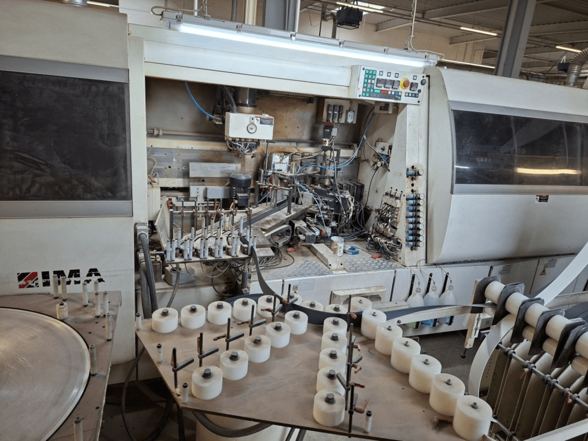 Les machines IMA vues de côté, présentant des composants mécaniques complexes et une table ronde avec des bobines blanches.