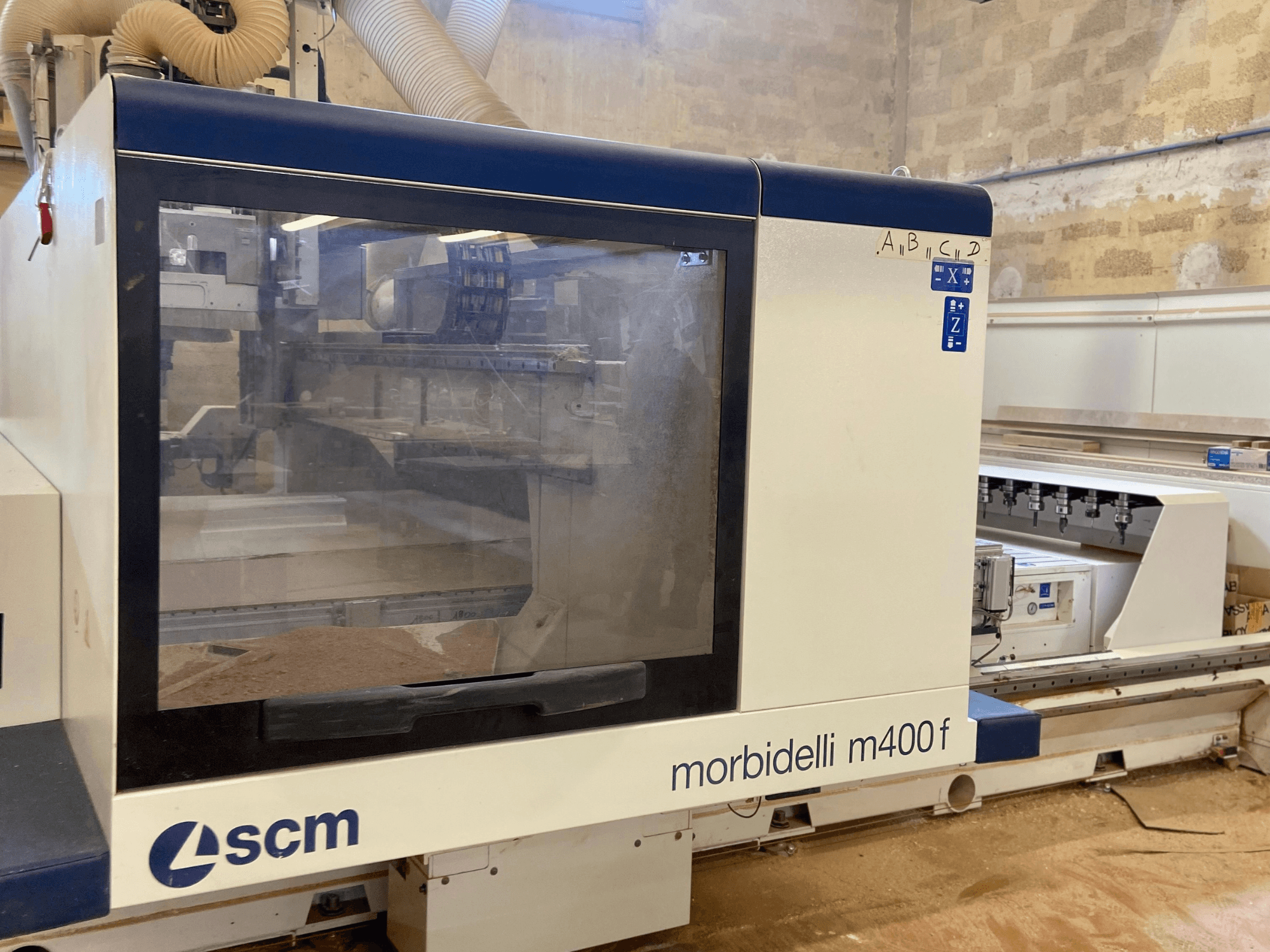 Machine CNC SCM Morbidelli M400F, vue de face, avec un panneau de commande et de la sciure de bois visible sur le sol.