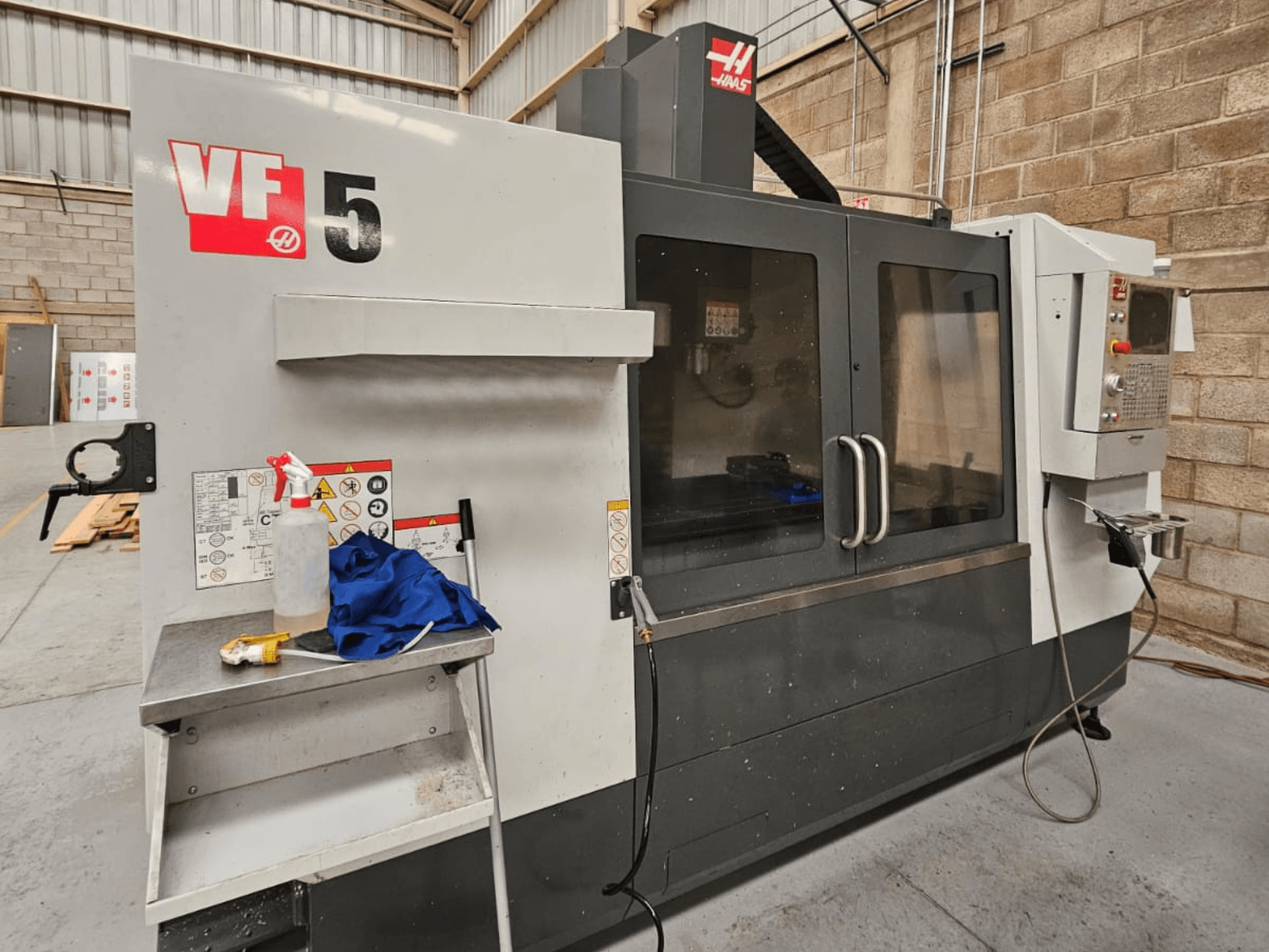 Fraiseuse CNC Haas VF-5 vue de face, avec panneau de commande, bouteille de liquide de refroidissement, chiffon bleu et consignes de sécurité.