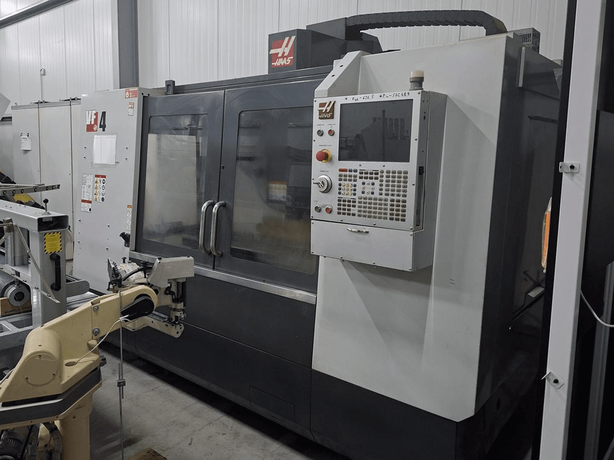 Fraiseuse CNC Haas VF-4 vue de face, dotée d'un panneau de commande numérique et d'un bras robotisé pour l'automatisation.