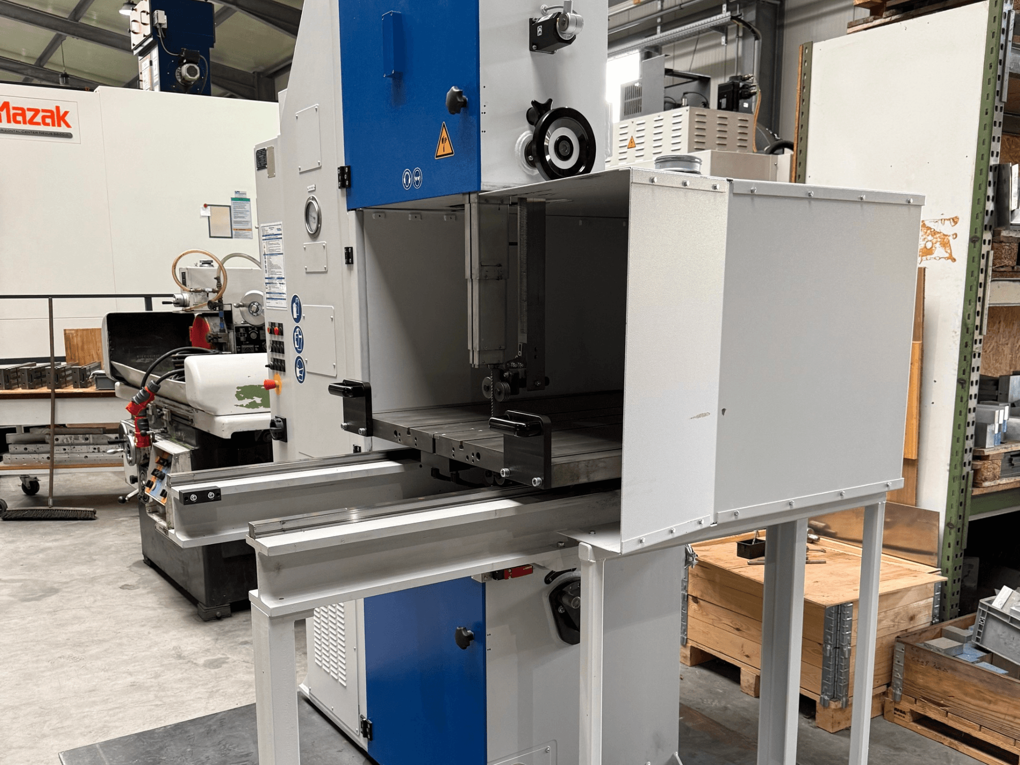 Machine industrielle Mazak vue de face, avec un panneau de commande bleu, une table métallique et des avertissements de sécurité.