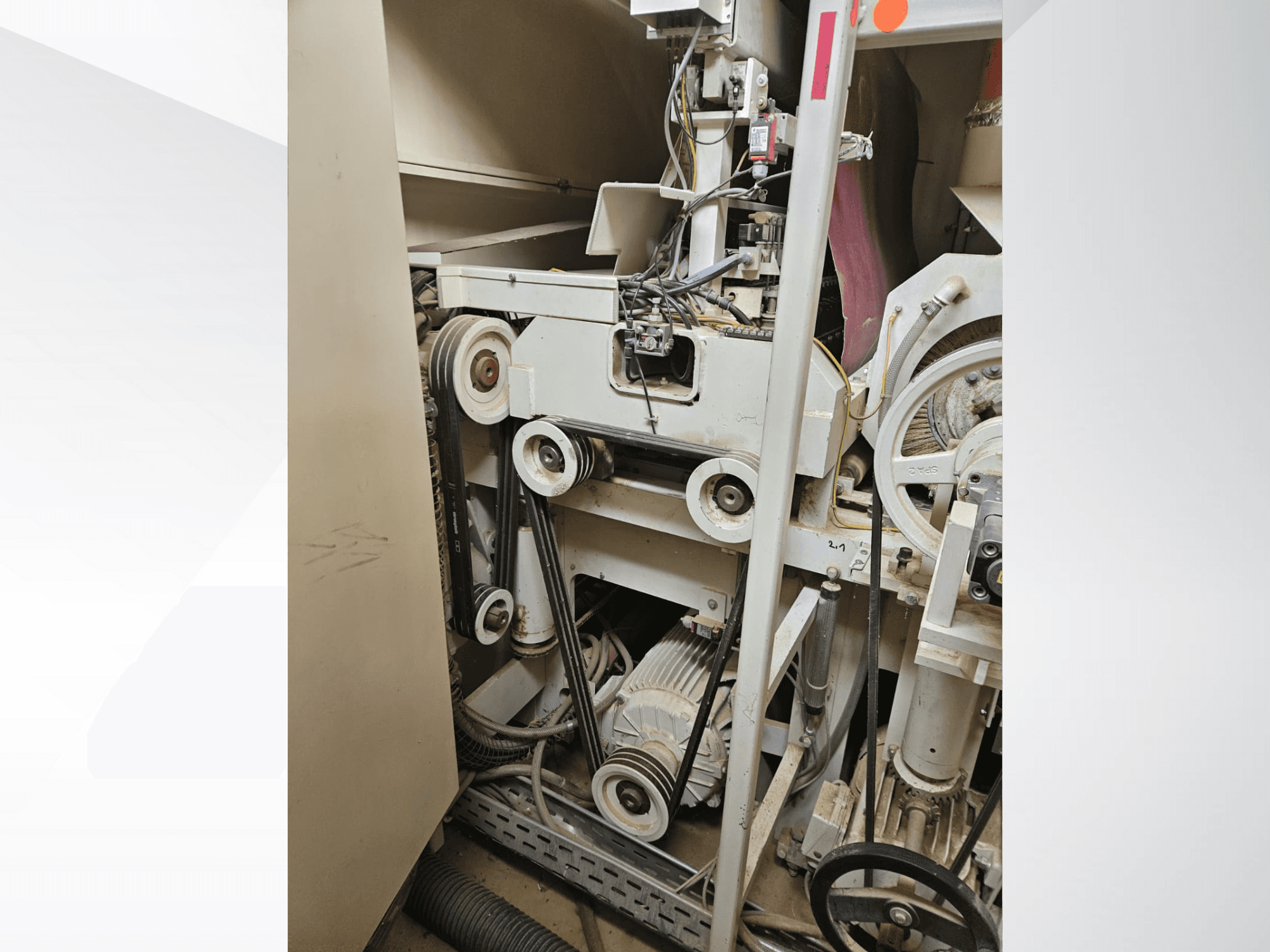 Intérieur d'une machine industrielle à courroies et poulies, avec moteur et câblage, vue de côté.