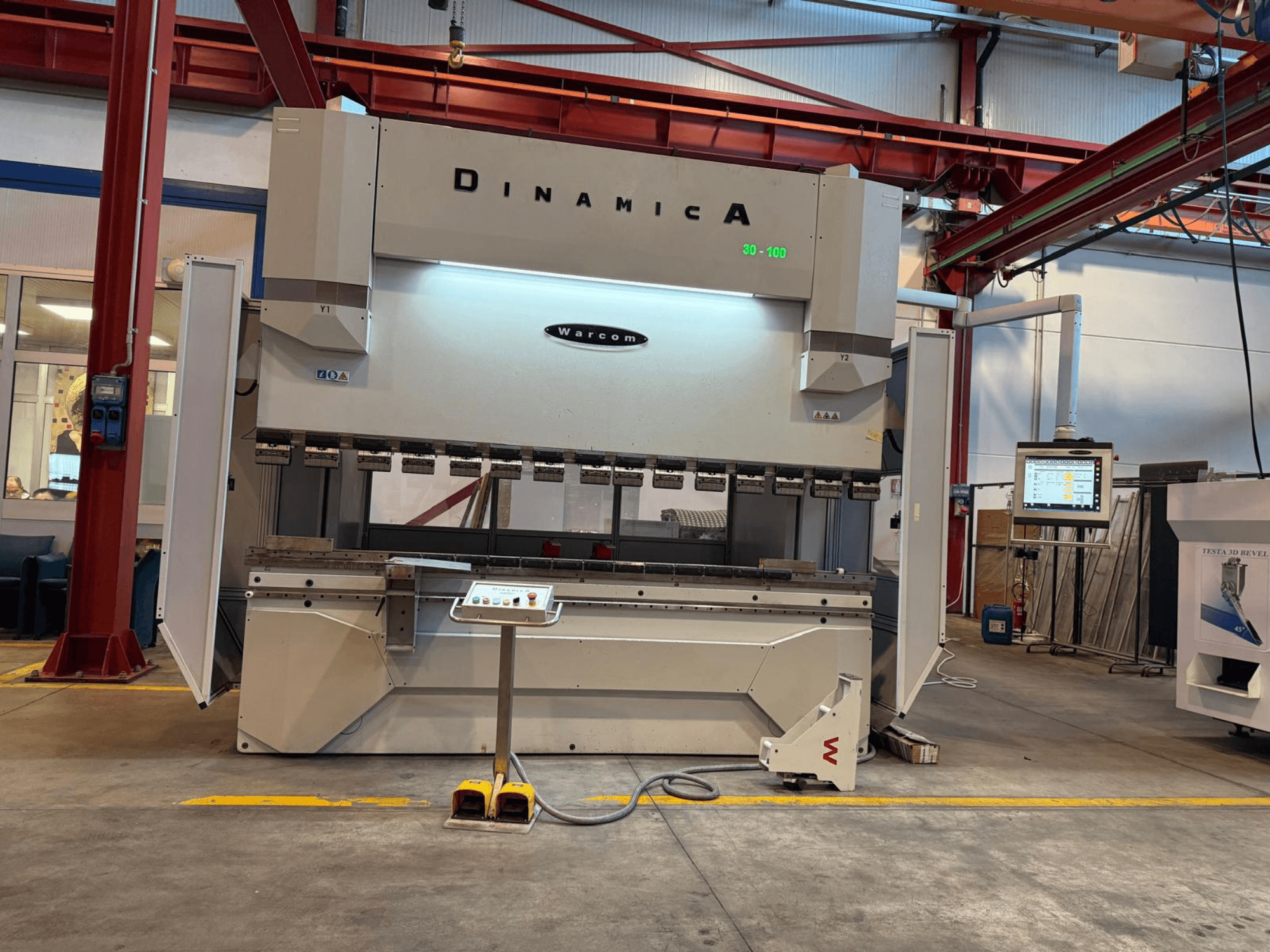 Presse plieuse hydraulique Dinamica Warcom, vue de face. Comprend un panneau de commande et plusieurs stations d'outillage pour un pliage de précision.