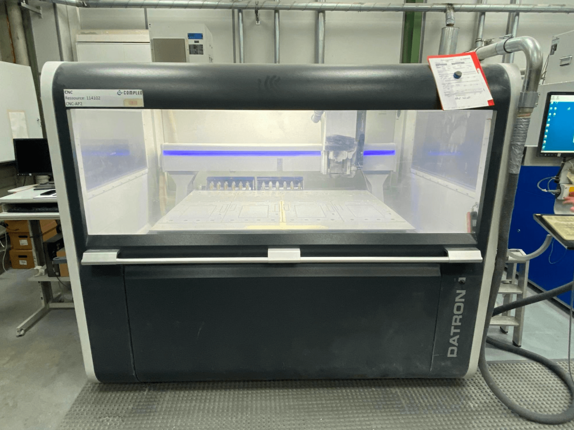 Vue de face d'un centre d'usinage vertical Datron MLCube B, avec des commandes visibles et une table de travail, dans un atelier.