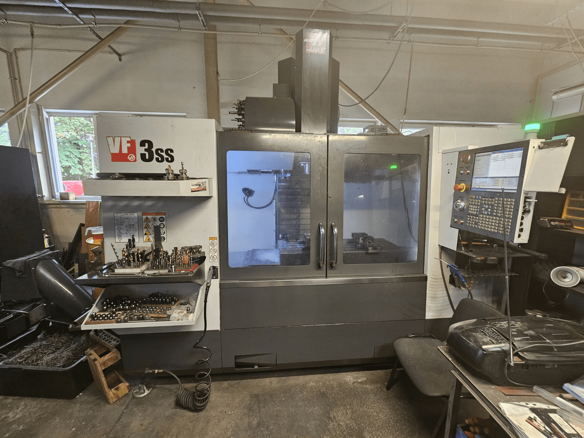 Centre d'usinage vertical Haas VF-3SS dans un atelier, vue de face montrant le panneau de commande et le compartiment de rangement des outils.