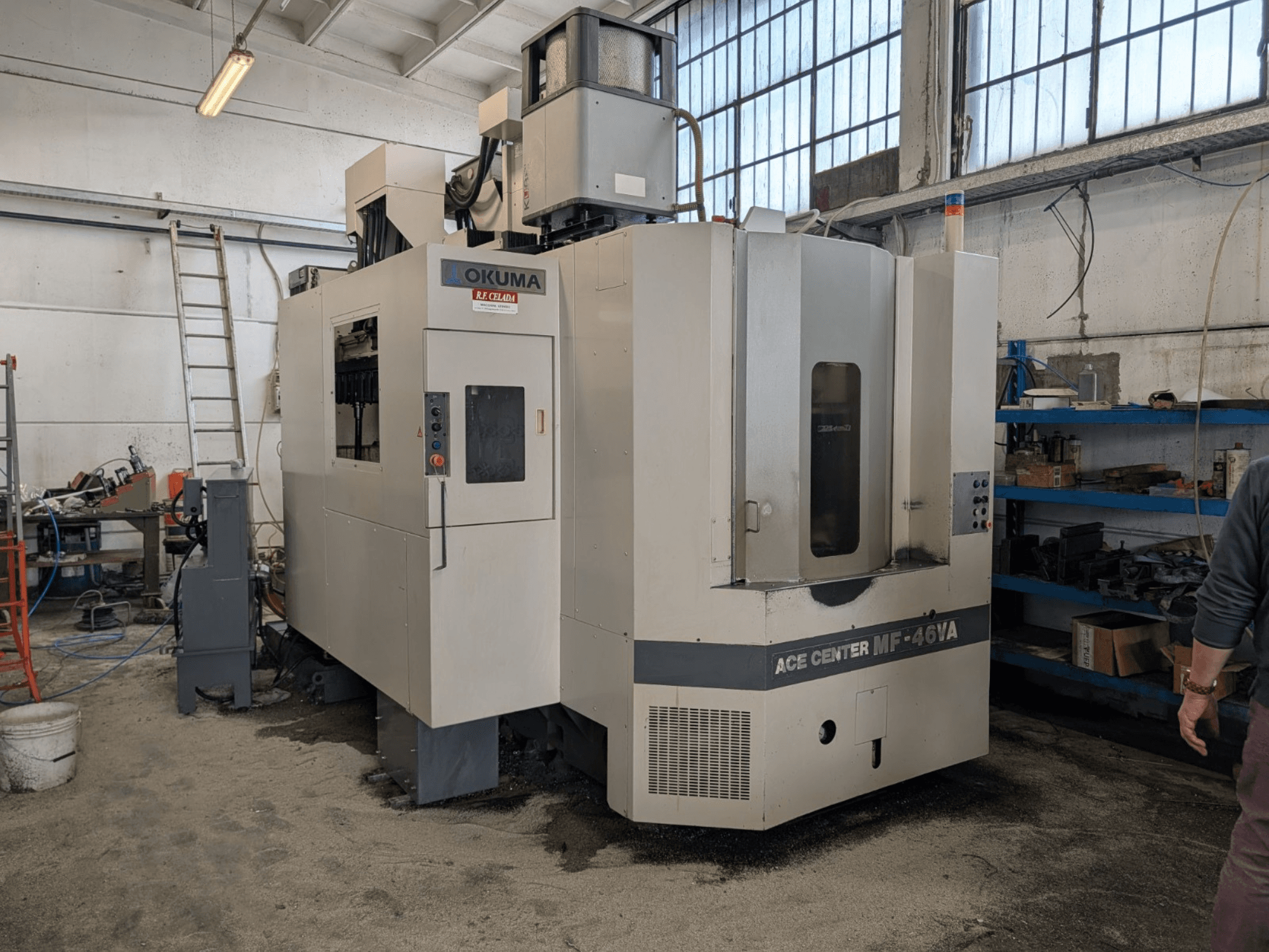 Centre d'usinage vertical Okuma ACE CENTER MF-46VA dans un atelier, montrant la vue de face avec le panneau de commande et l'équipement environnant.