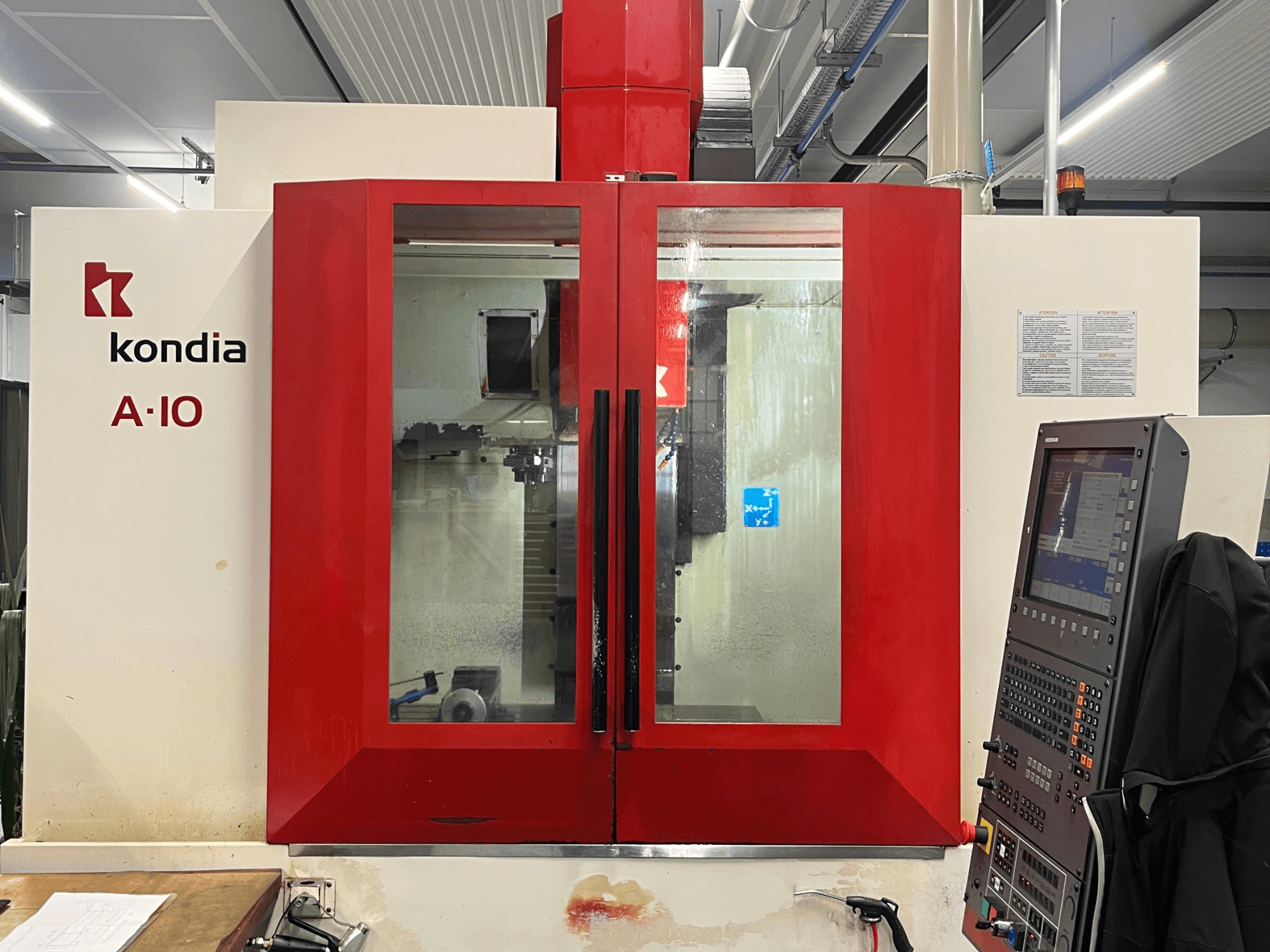 Centre d'usinage vertical KONDIA A10, vue de face ; portes en verre rouge et panneau de commande à droite.