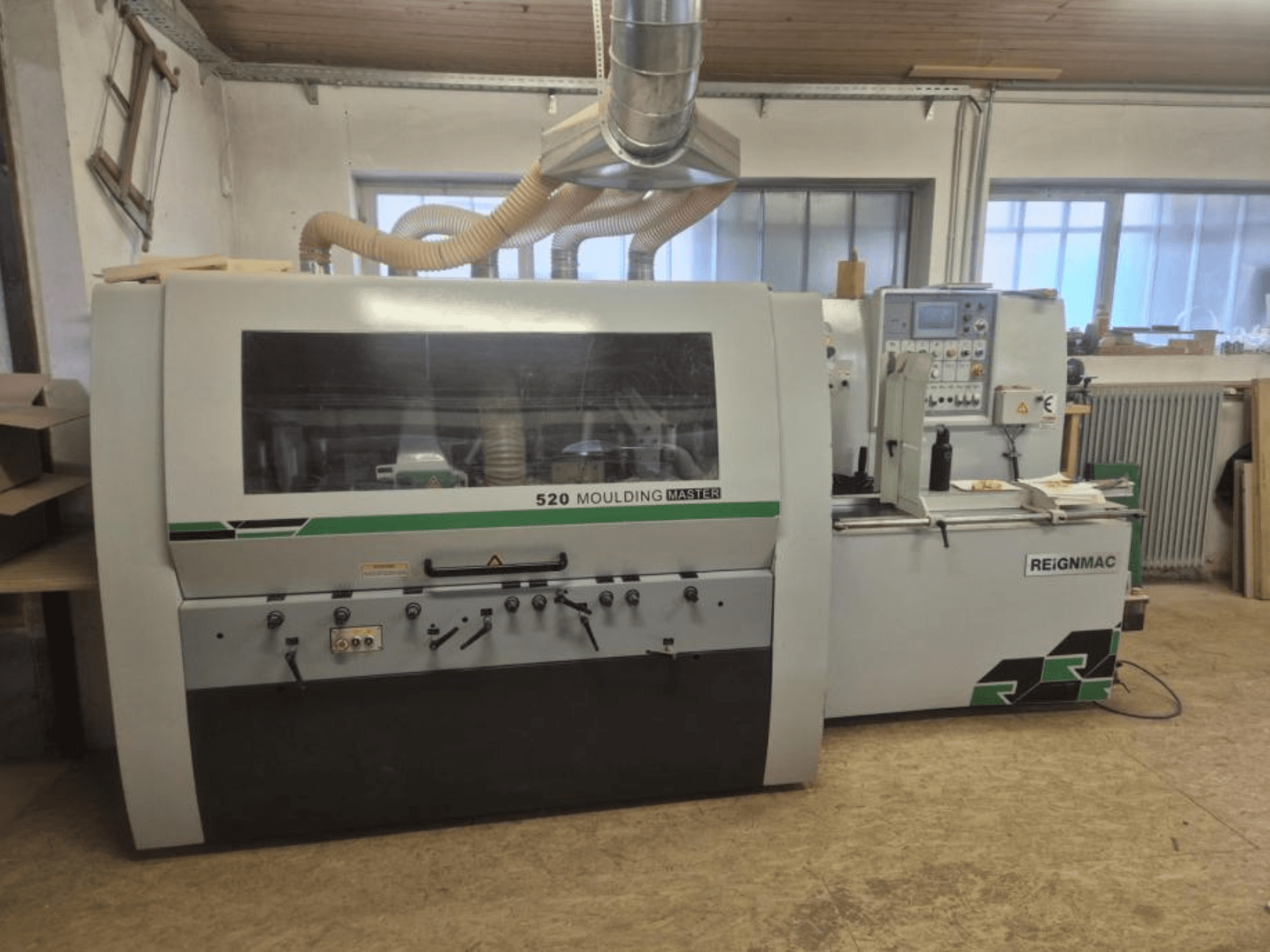 Vue avant de la raboteuse REIGNMAC 520 MOULDING MASTER, montrant le panneau de commande, les rouleaux d'alimentation et le système d'extraction des poussières.