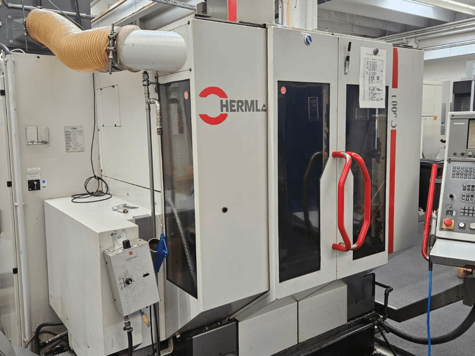 Vue de face du centre d'usinage universel HERMLE C 600 U, montrant le panneau de commande et les poignées rouges sur les portes.