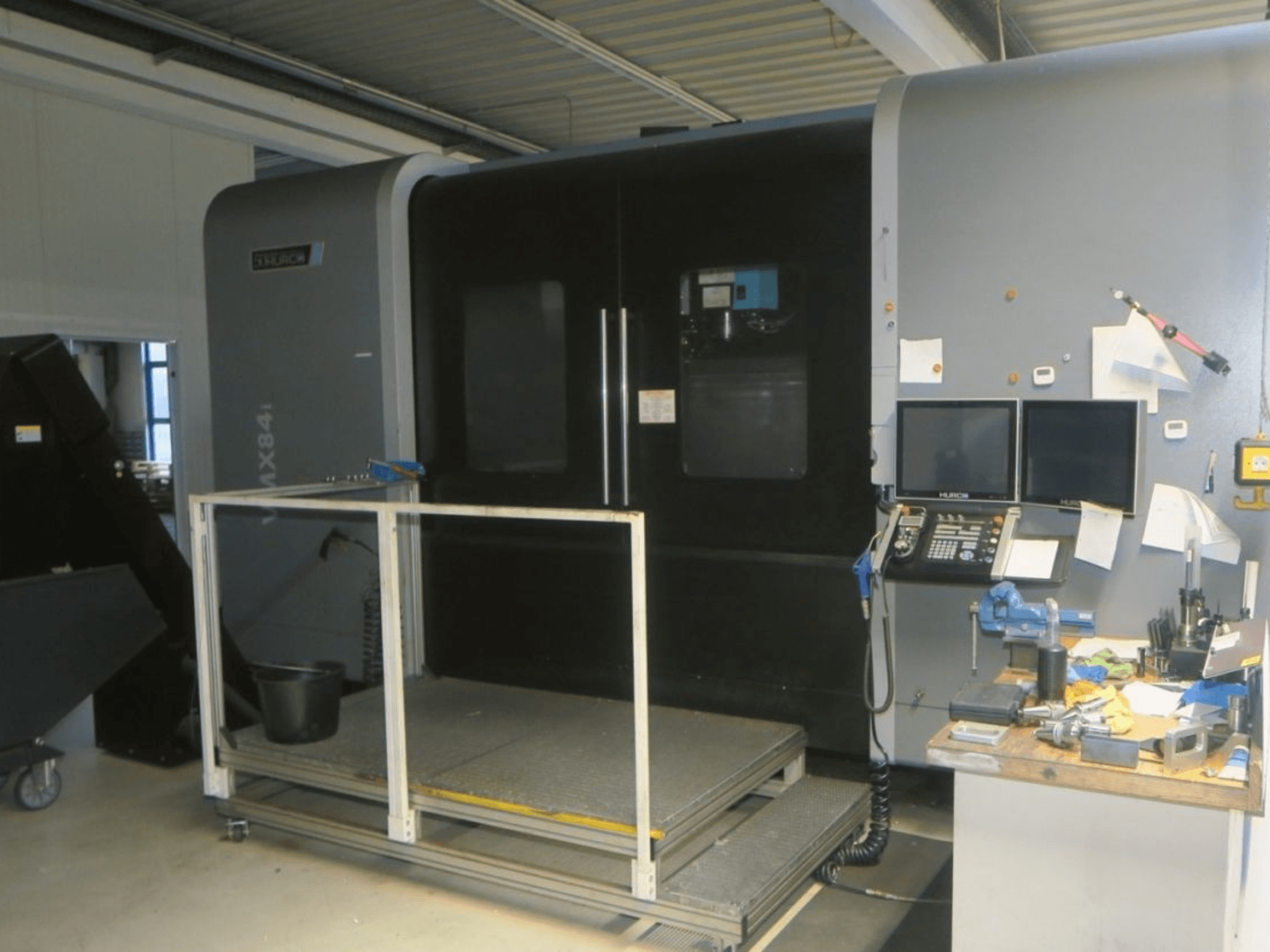 Machine CNC Hurco MX84 vue de face, montrant les deux moniteurs, le panneau de commande et l'espace de travail avec divers outils.
