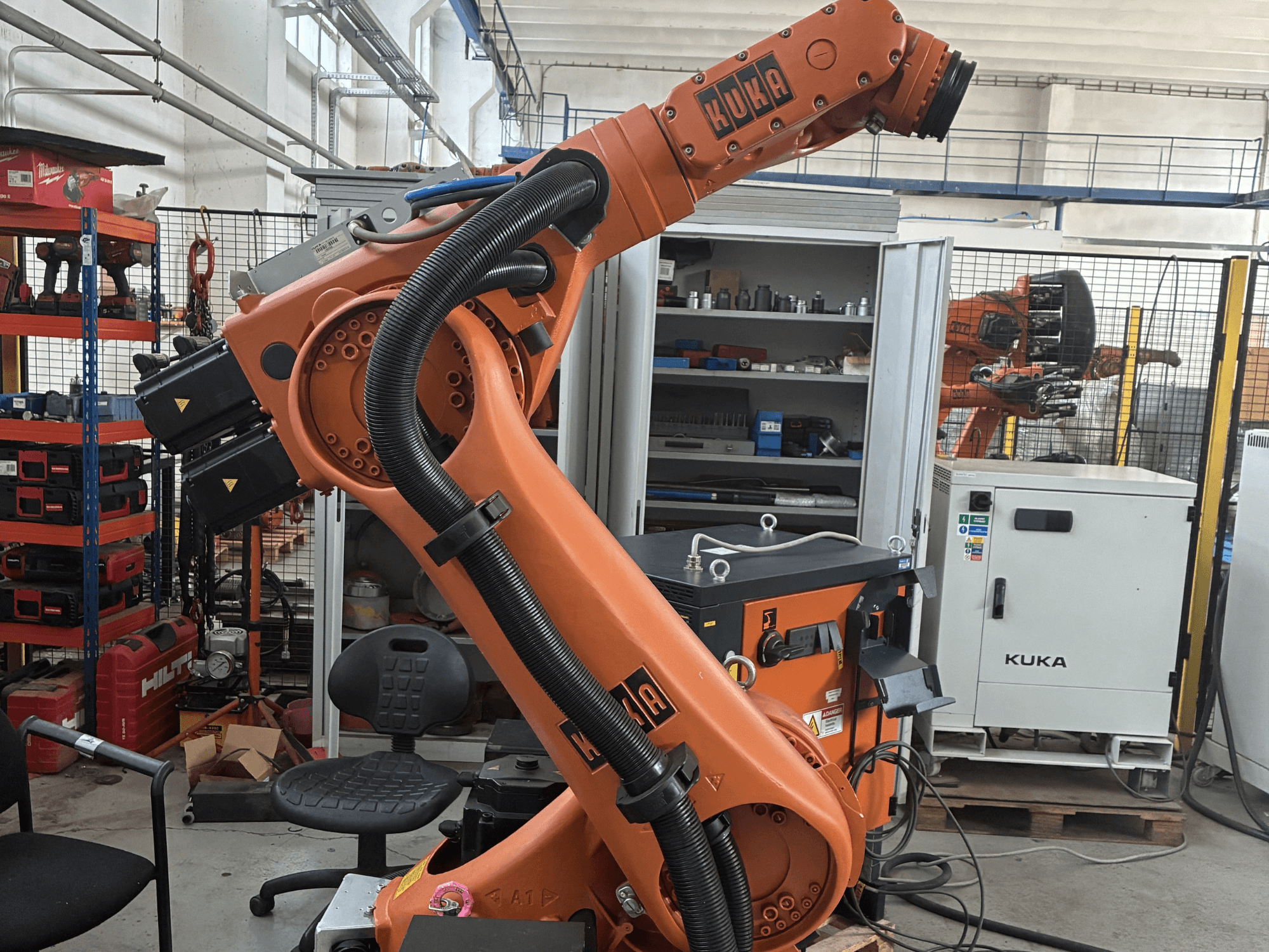Bras robotique KUKA KR30-3 dans un environnement industriel, vue latérale montrant les câbles et les commandes, avec des outils et des étagères en arrière-plan.