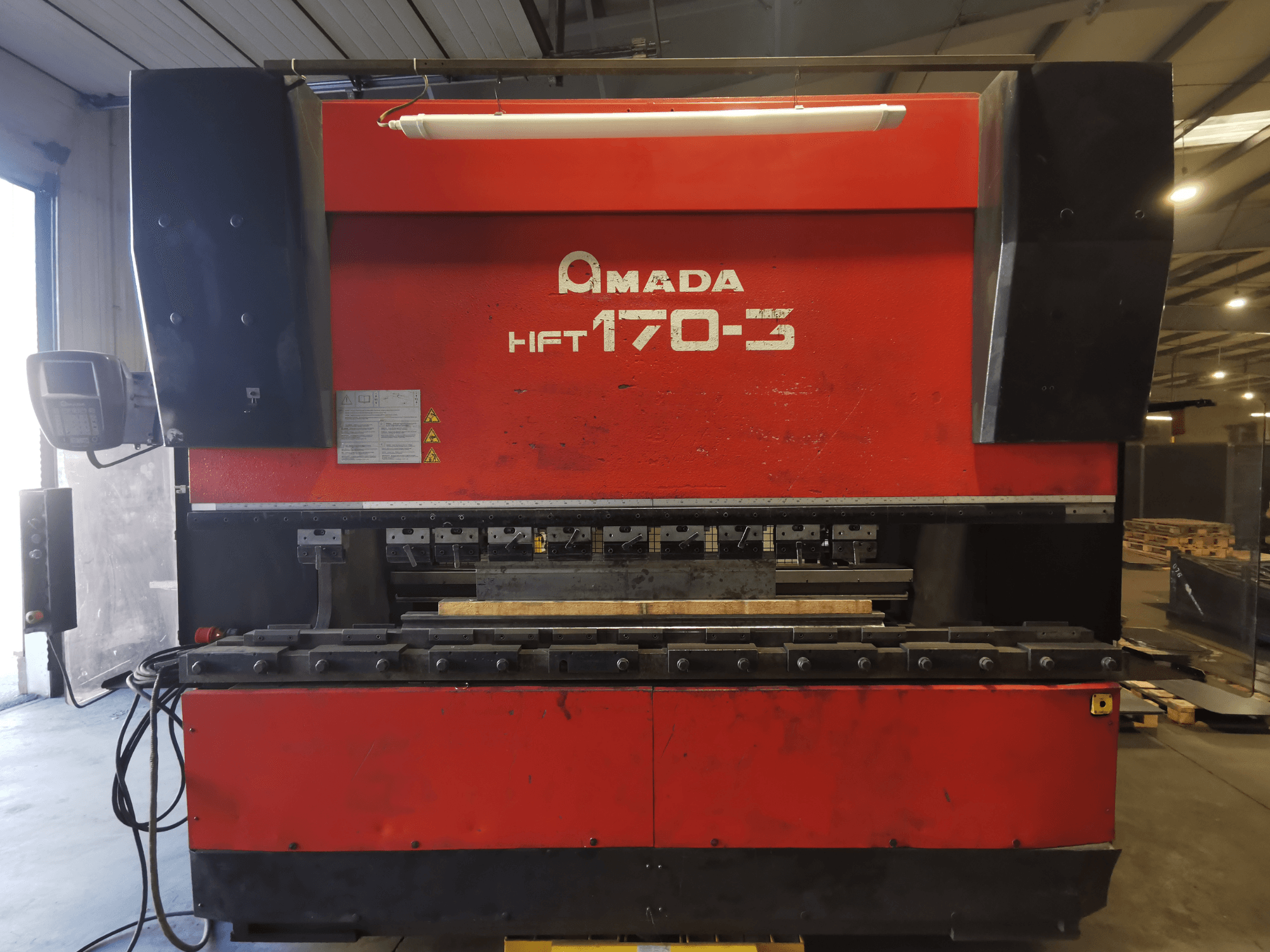 Presse plieuse Amada HFT 170-3 rouge vue de face, montrant le panneau de commande, les outils de pliage et la surface de travail.