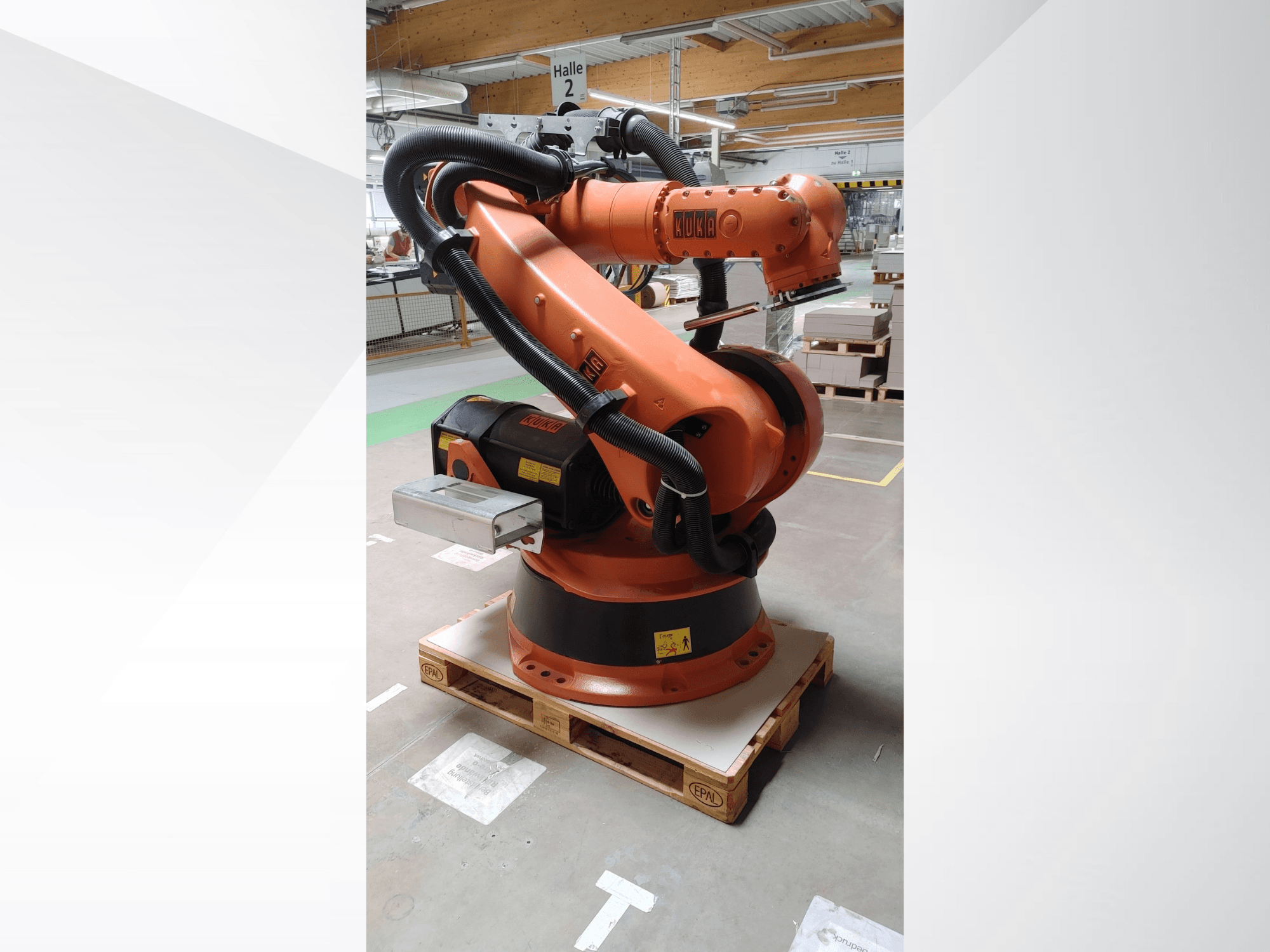 Bras robotique KUKA KR140-3 COMP en orange, vue de face sur une palette en bois, avec bras courbé et boîtier de commande.