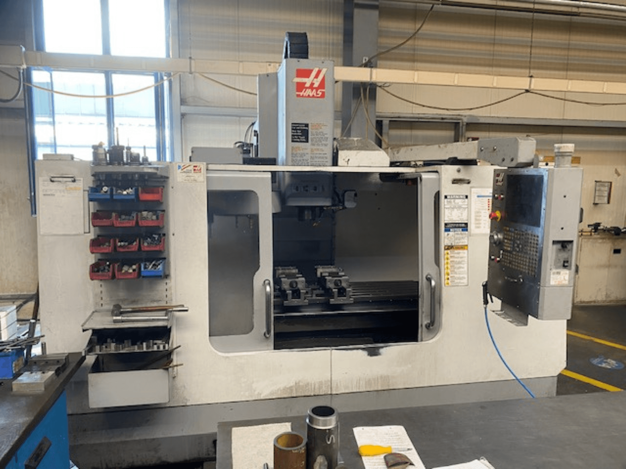 Vue de face de la fraiseuse CNC Haas, modèle VF-2, avec le rangement des outils, le panneau de commande et les outils de l'espace de travail visibles.