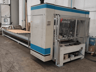 La machine ERREBI, vue de côté, comporte une grande table de traitement avec des composants mécaniques et un couvercle de protection transparent.